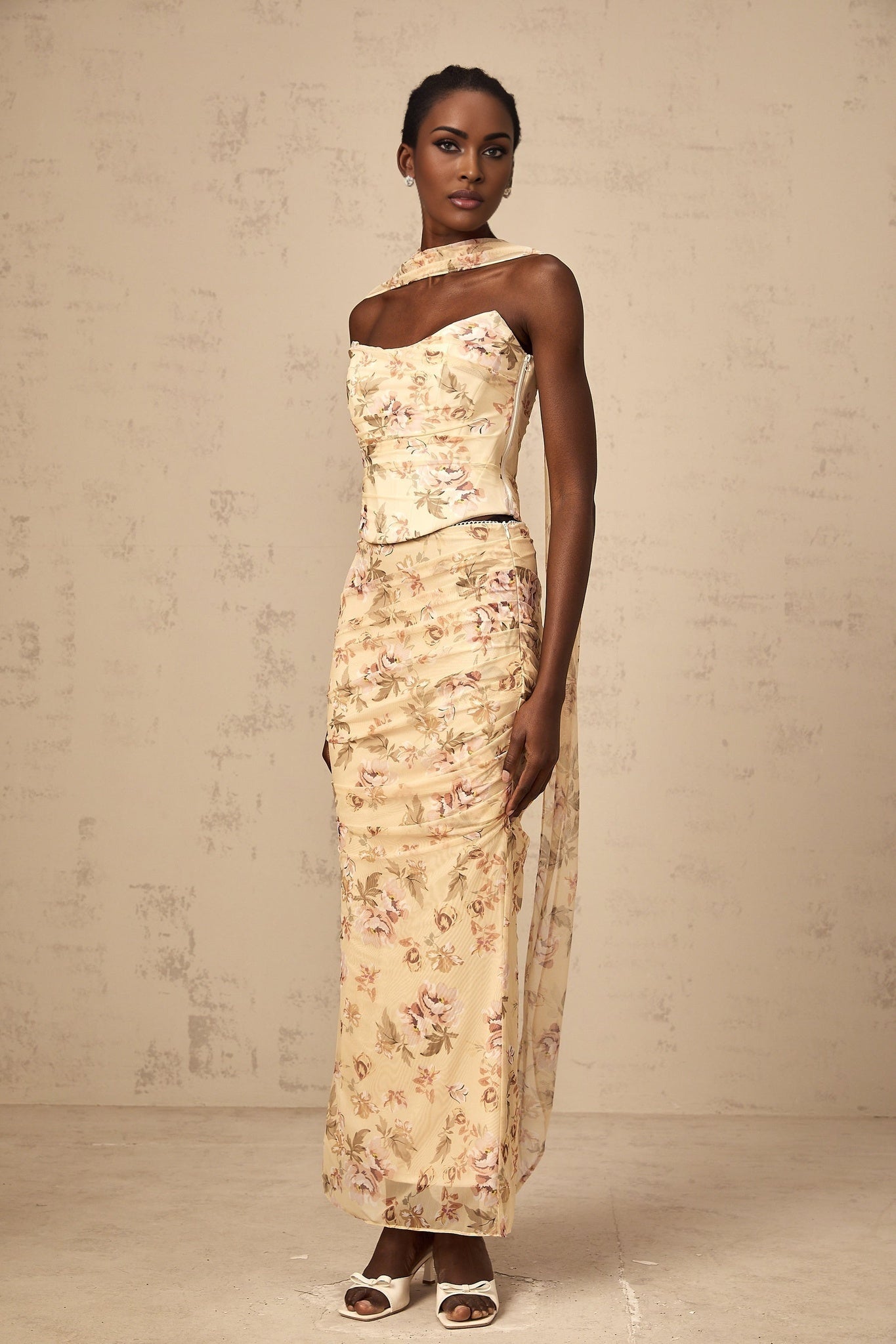 A woman wearing a bright yellow floral print matching set consisting of a fitted top and skirt standing against a plain background