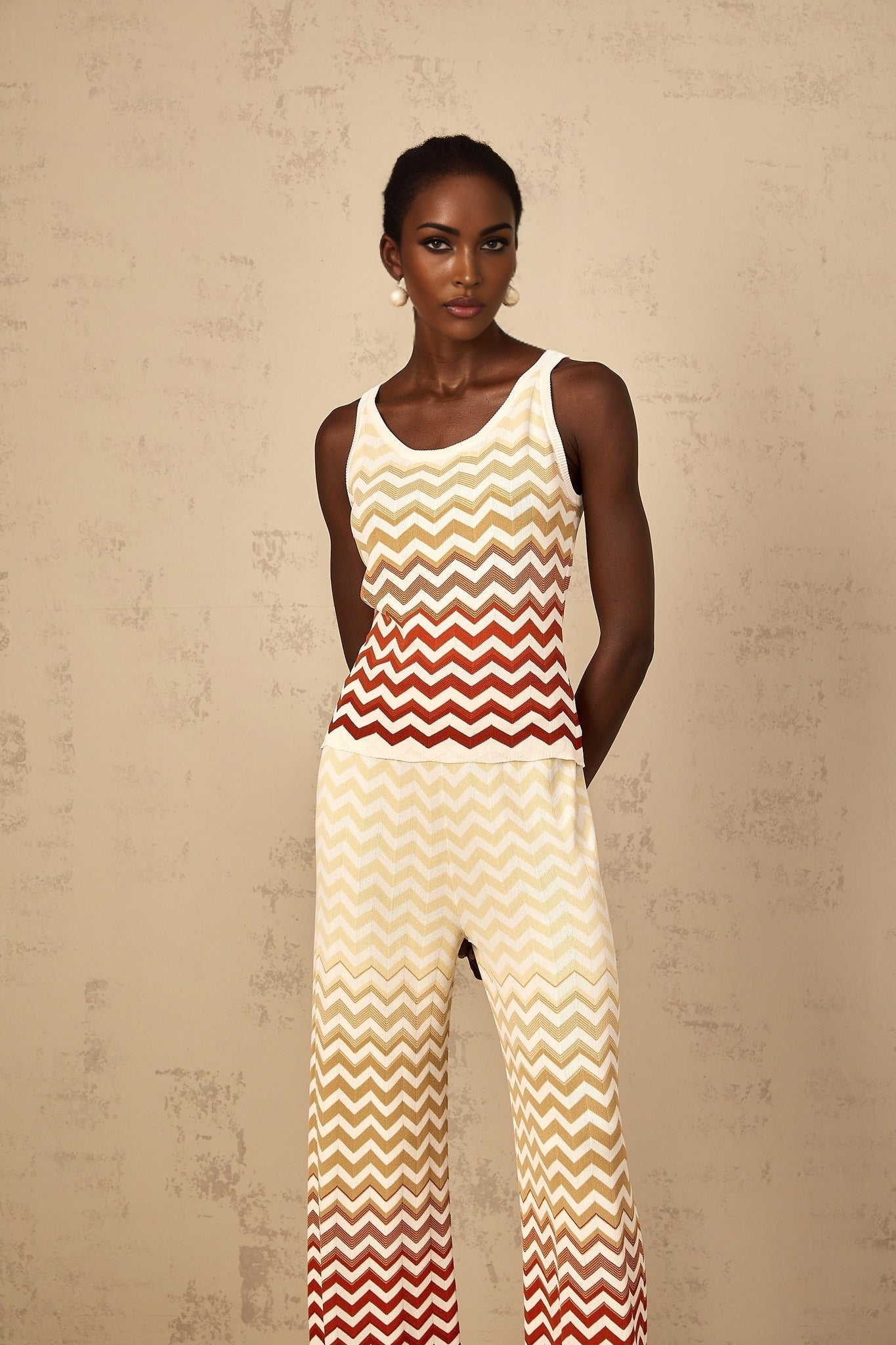 A woman wearing a bright yellow knit two piece outfit with a zigzag pattern consisting of a cropped top and matching bottoms