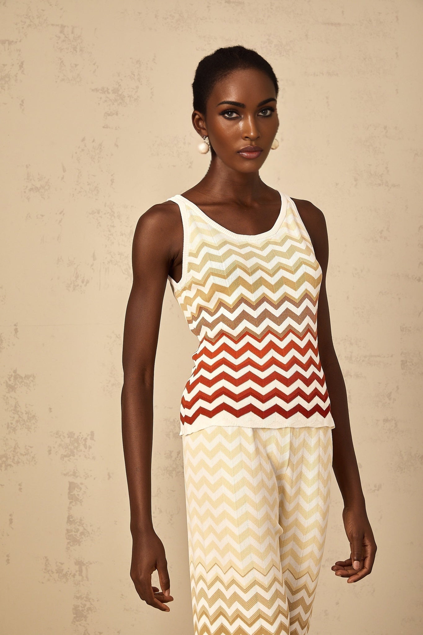 A woman wearing a bright yellow knit two piece set featuring a zigzag pattern The top is sleeveless and cropped while the bottoms are fitted shorts The outfit is displayed on a model against a plain background