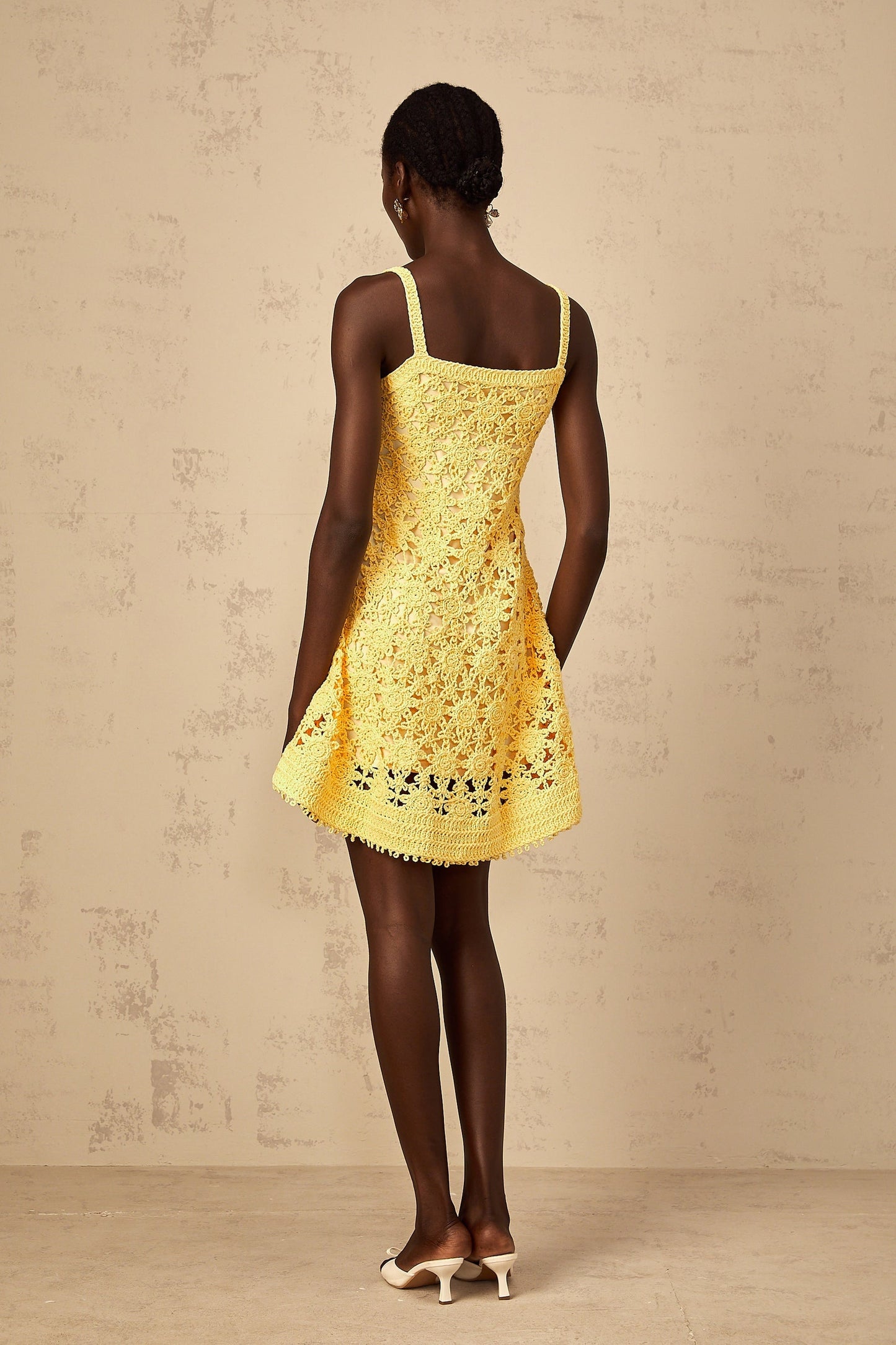 A woman wearing a bright yellow mini dress with a flared skirt and crochet knit pattern standing against a plain background