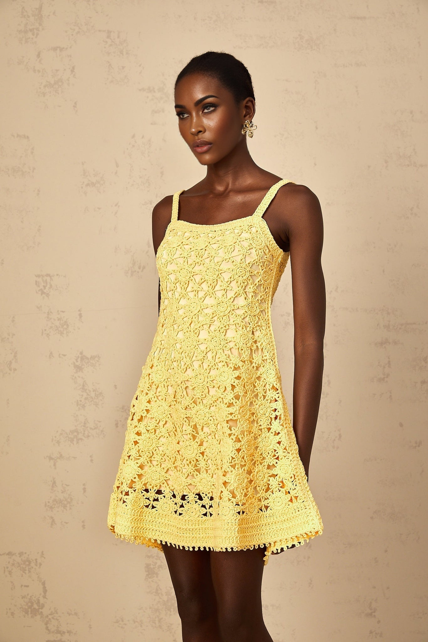A woman wearing a bright yellow mini dress with a flared skirt and crochet knit pattern standing against a plain background