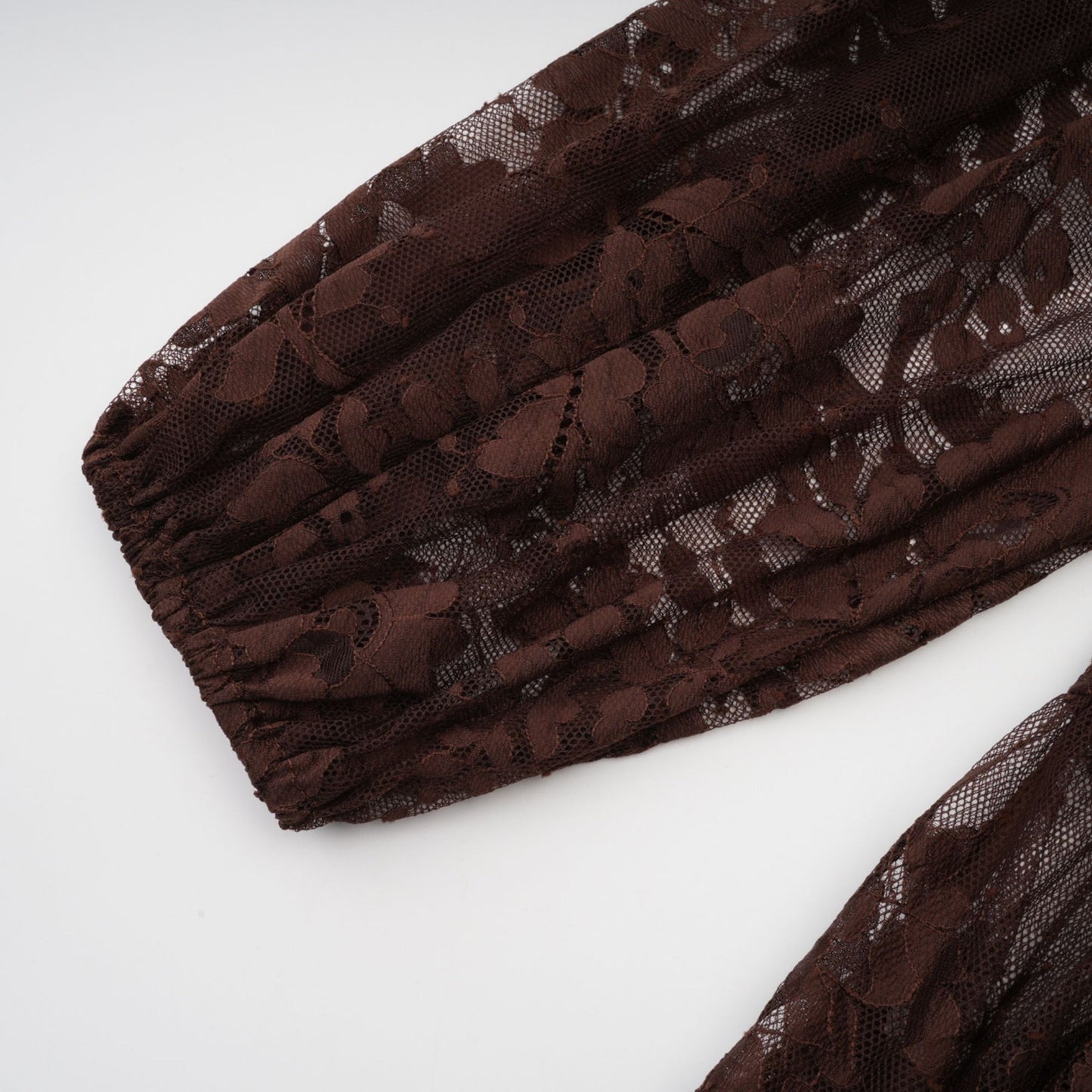 A woman wearing a brown flared midi dress made of chantilly lace named Sylvie the dress features delicate floral patterns and a fitted bodice with a flowy skirt that falls to mid calf length