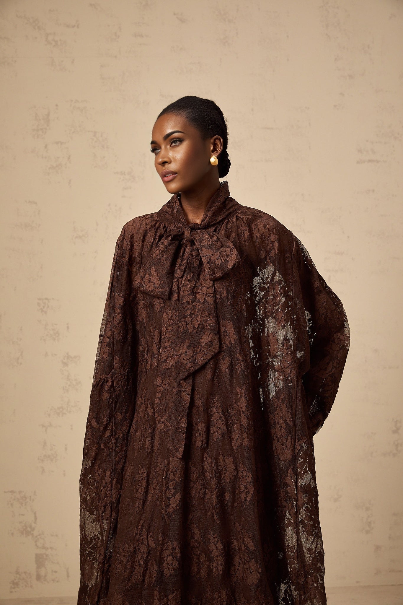 A woman wearing a brown flared midi dress made of chantilly lace with a fitted bodice and flowing skirt