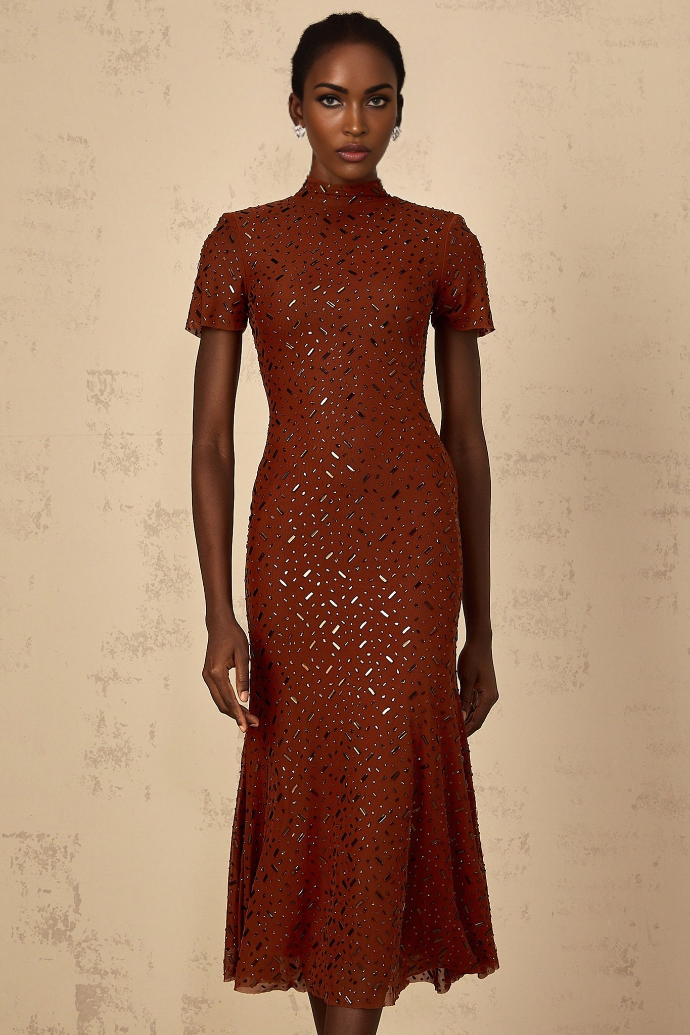 A woman wearing a brown midi dress with a flared tulle skirt and embellished details standing in a neutral pose