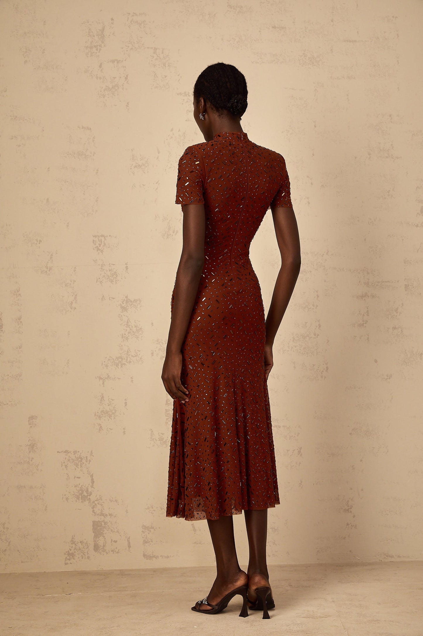 A woman wearing a brown midi dress with embellishments and a flared tulle skirt