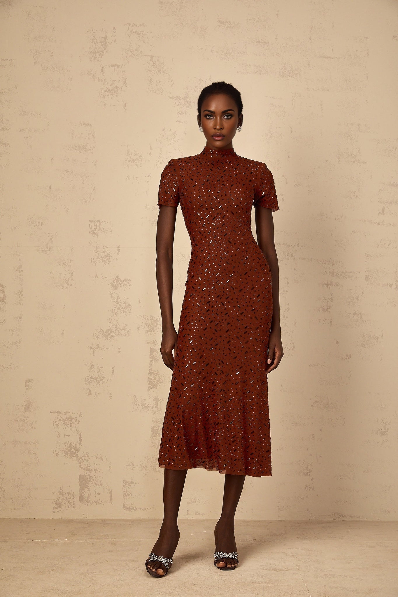 A woman wearing a brown midi dress with embellishments and a flared tulle skirt