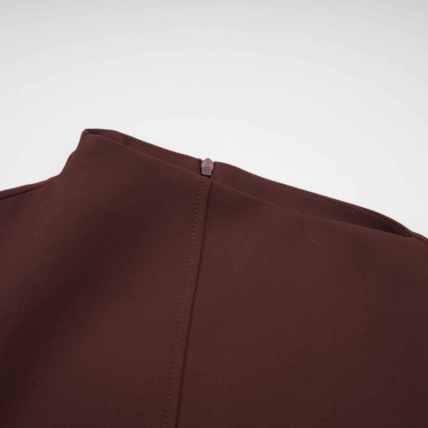 A woman wearing a brown mini dress with an asymmetric neckline and puff sleeves standing against a plain background