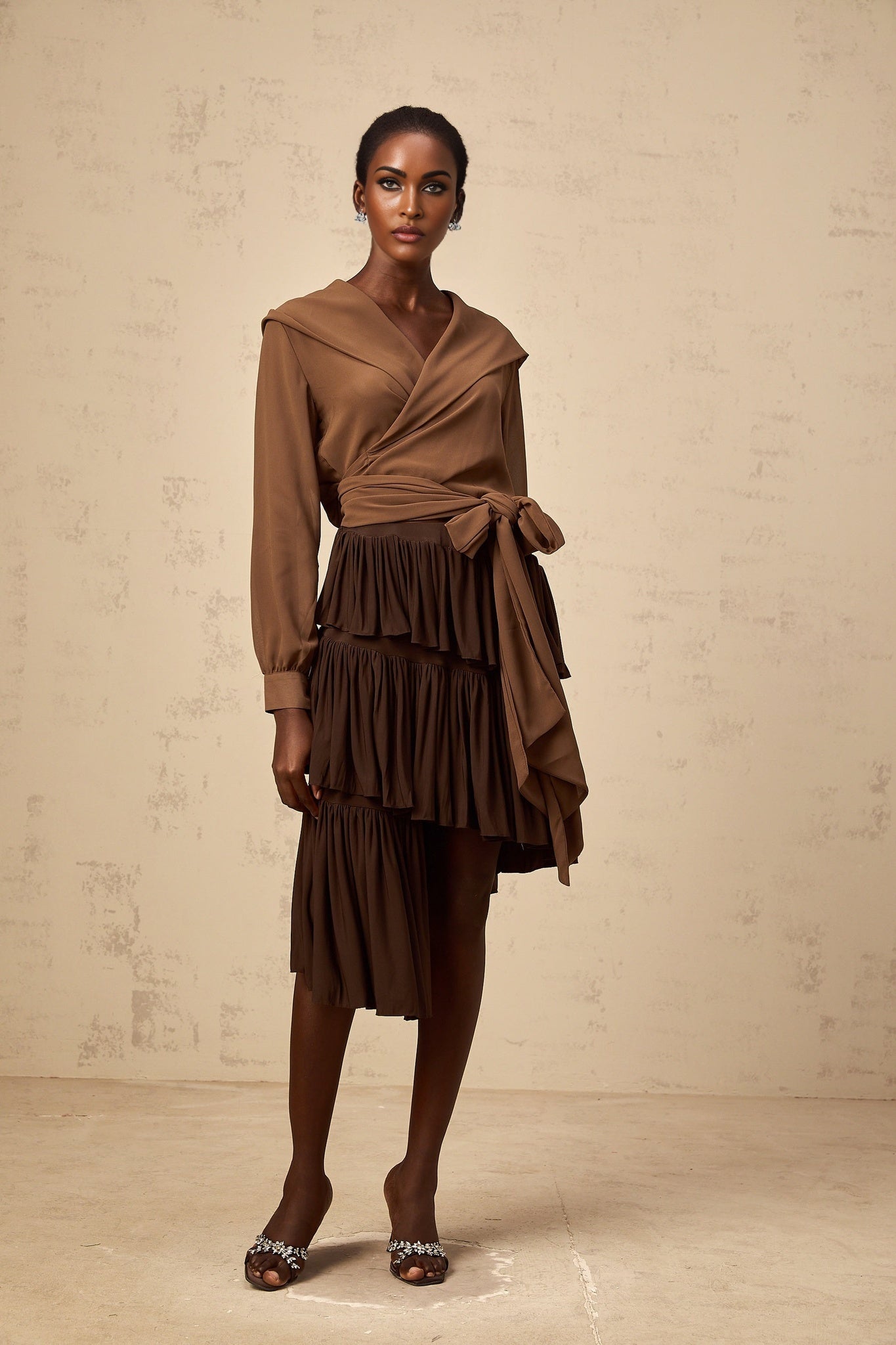 A woman wearing a brown semisheer hooded wrap top with long sleeves and a flowing silhouette