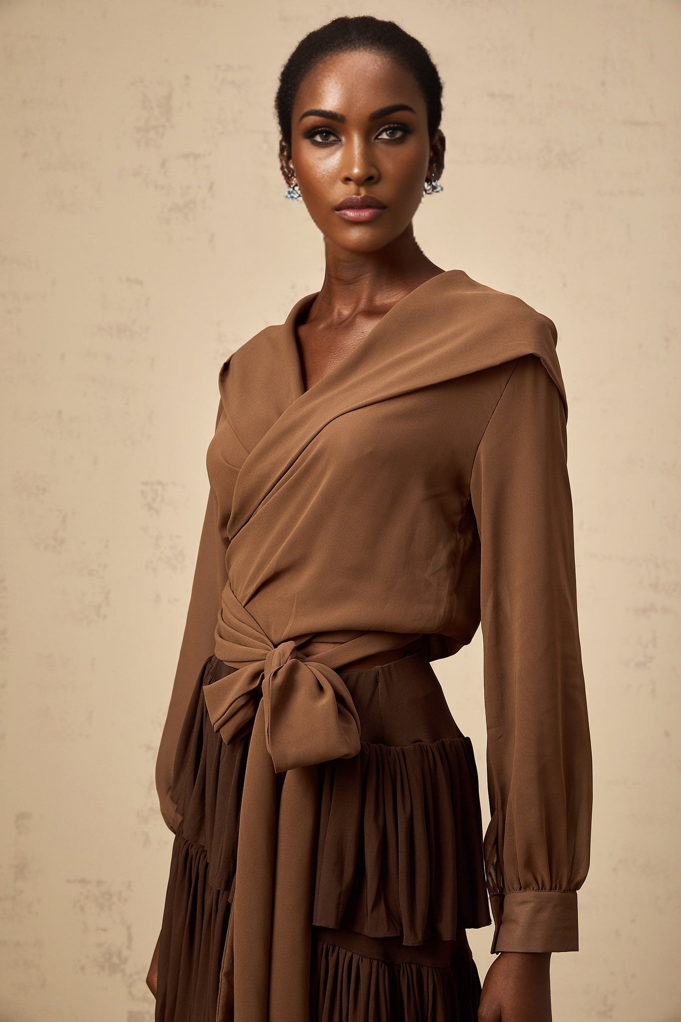 A woman wearing a brown semisheer hooded wrap top with long sleeves and a flowy silhouette
