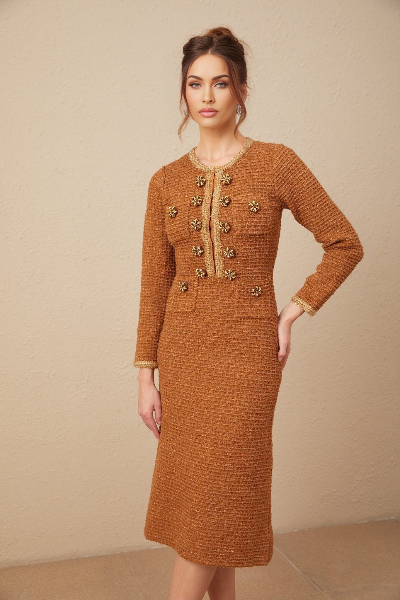A woman wearing a brown tweed dress with braided edges standing in a neutral background