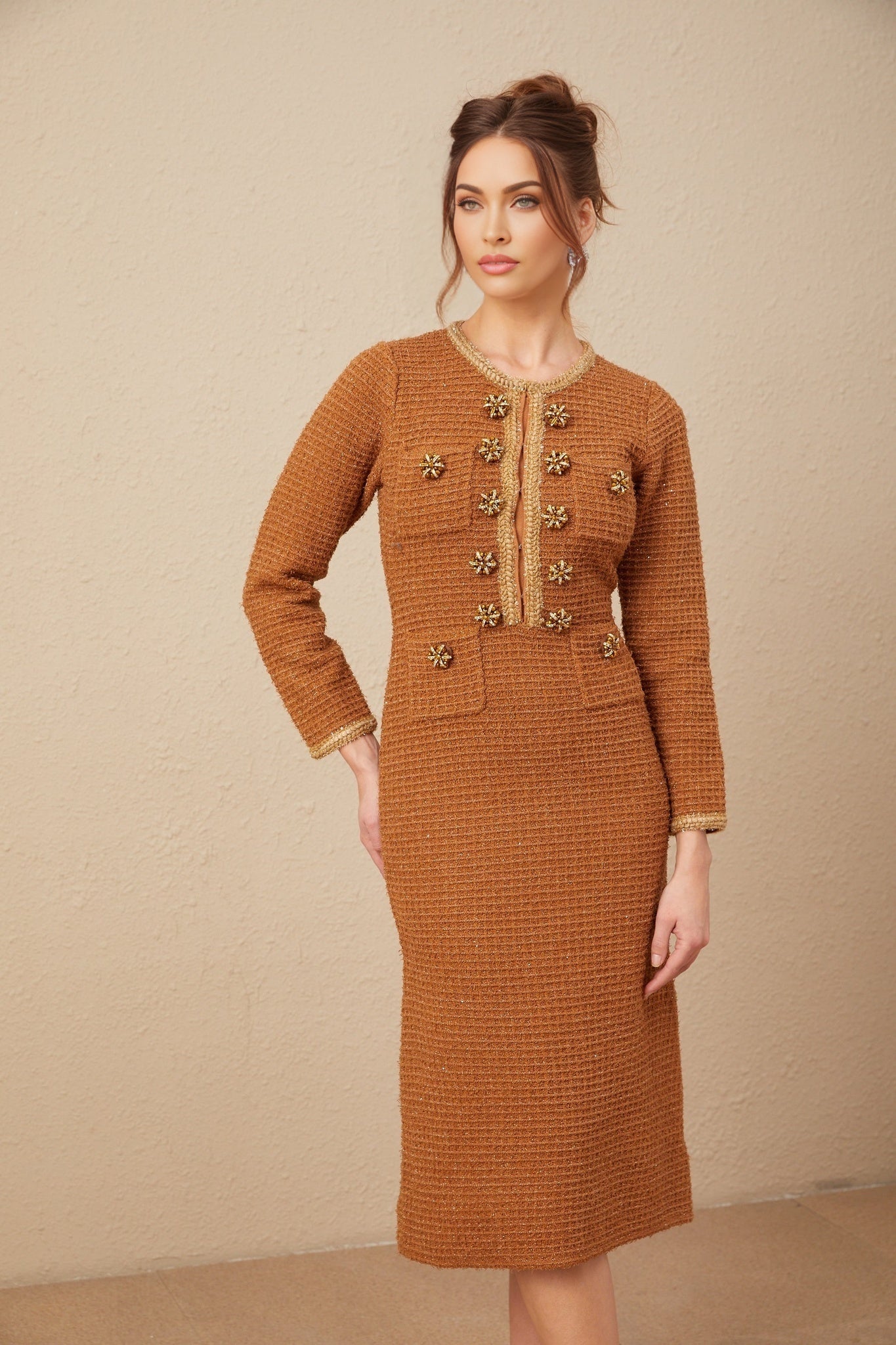 A woman wearing a brown tweed dress with braided edges standing in a neutral background