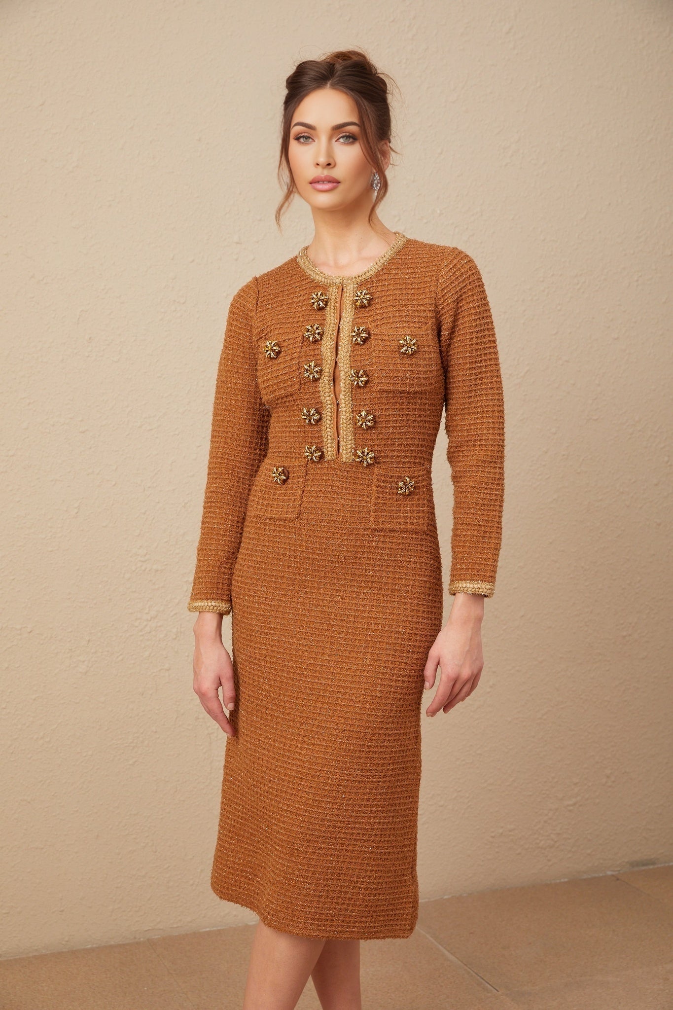 A woman wearing a brown tweed dress with braided edges standing in a neutral background