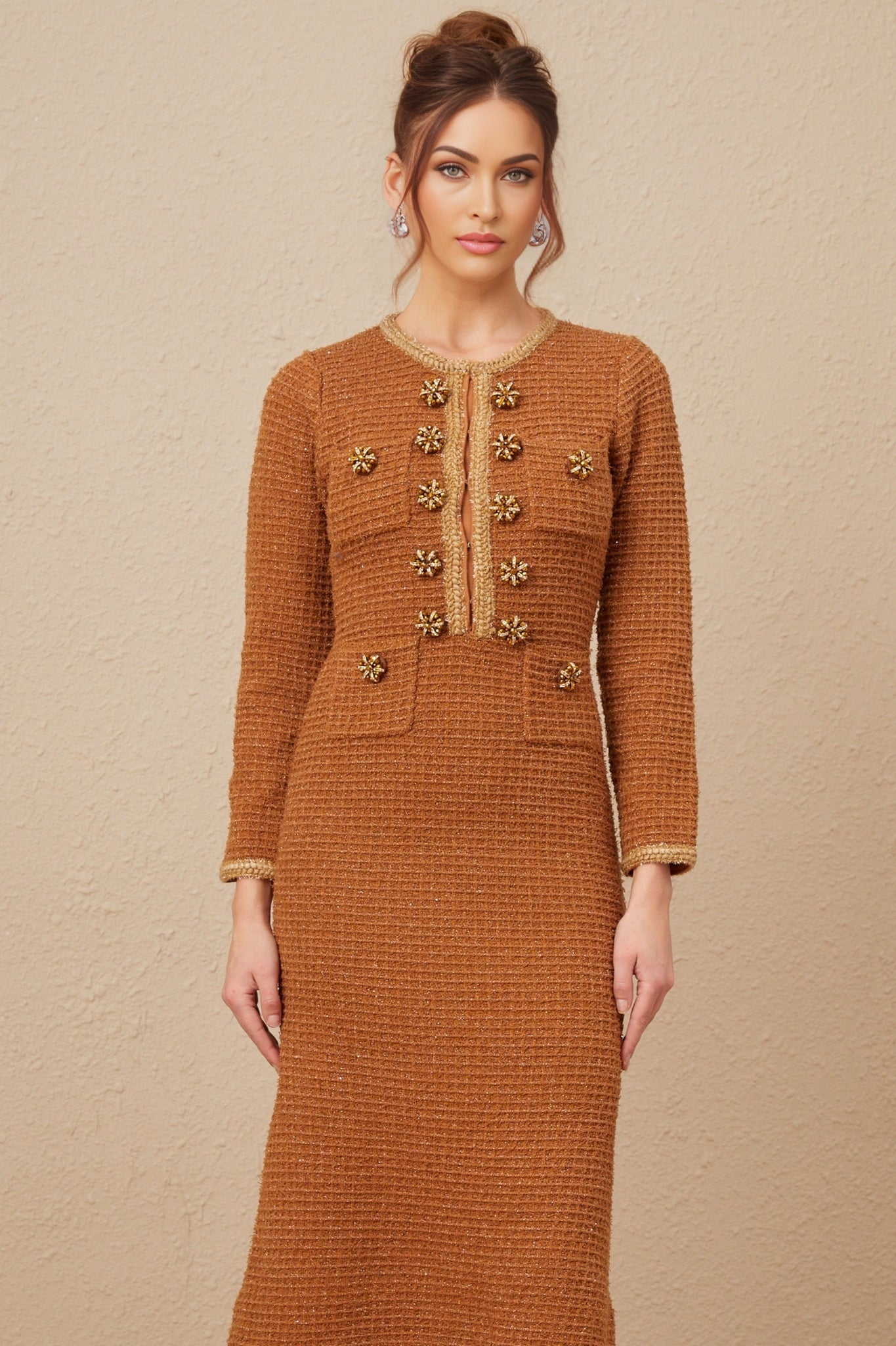 A woman wearing a brown tweed dress with braided edges standing in a neutral setting