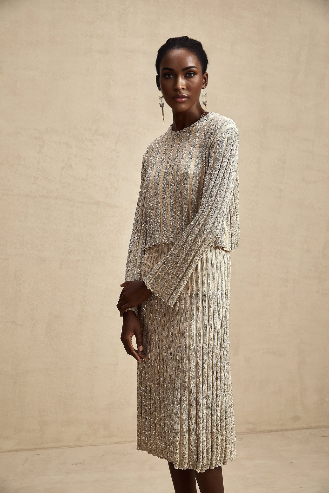 A woman wearing a champagne colored knit top and matching skirt with subtle vertical stripes The set has a soft and elegant appearance suitable for casual or semi formal occasions