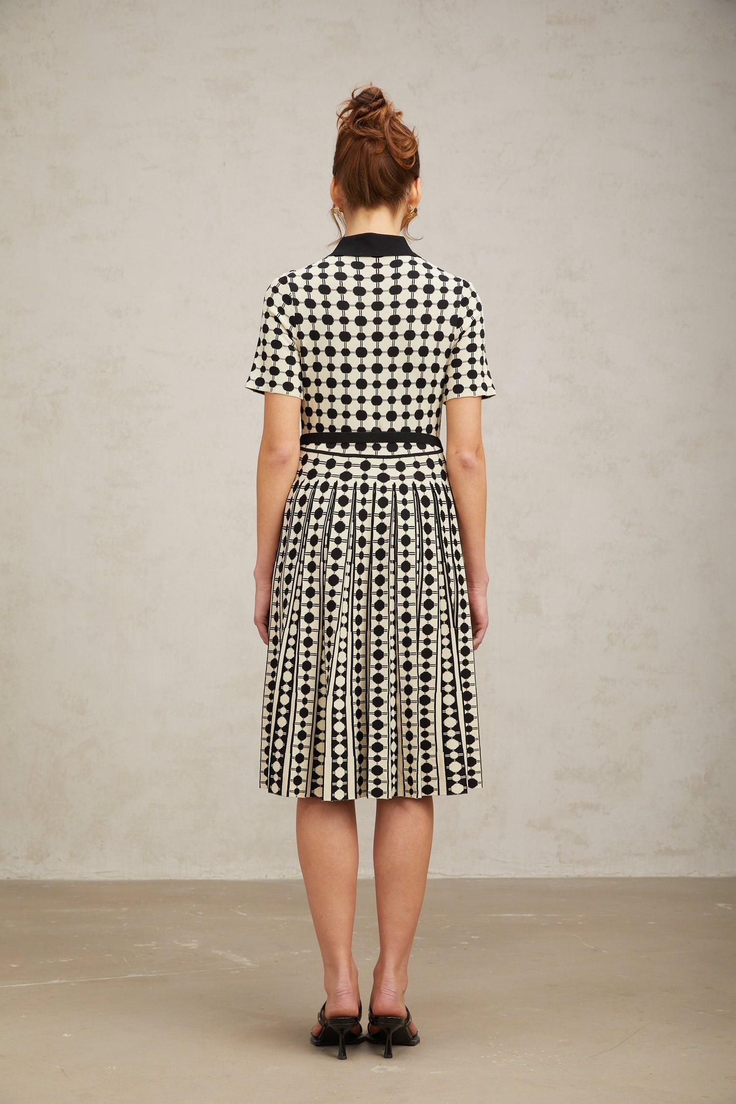 A woman wearing a colorblocked midi dress with polka dot pattern in contrasting colors standing against a plain background