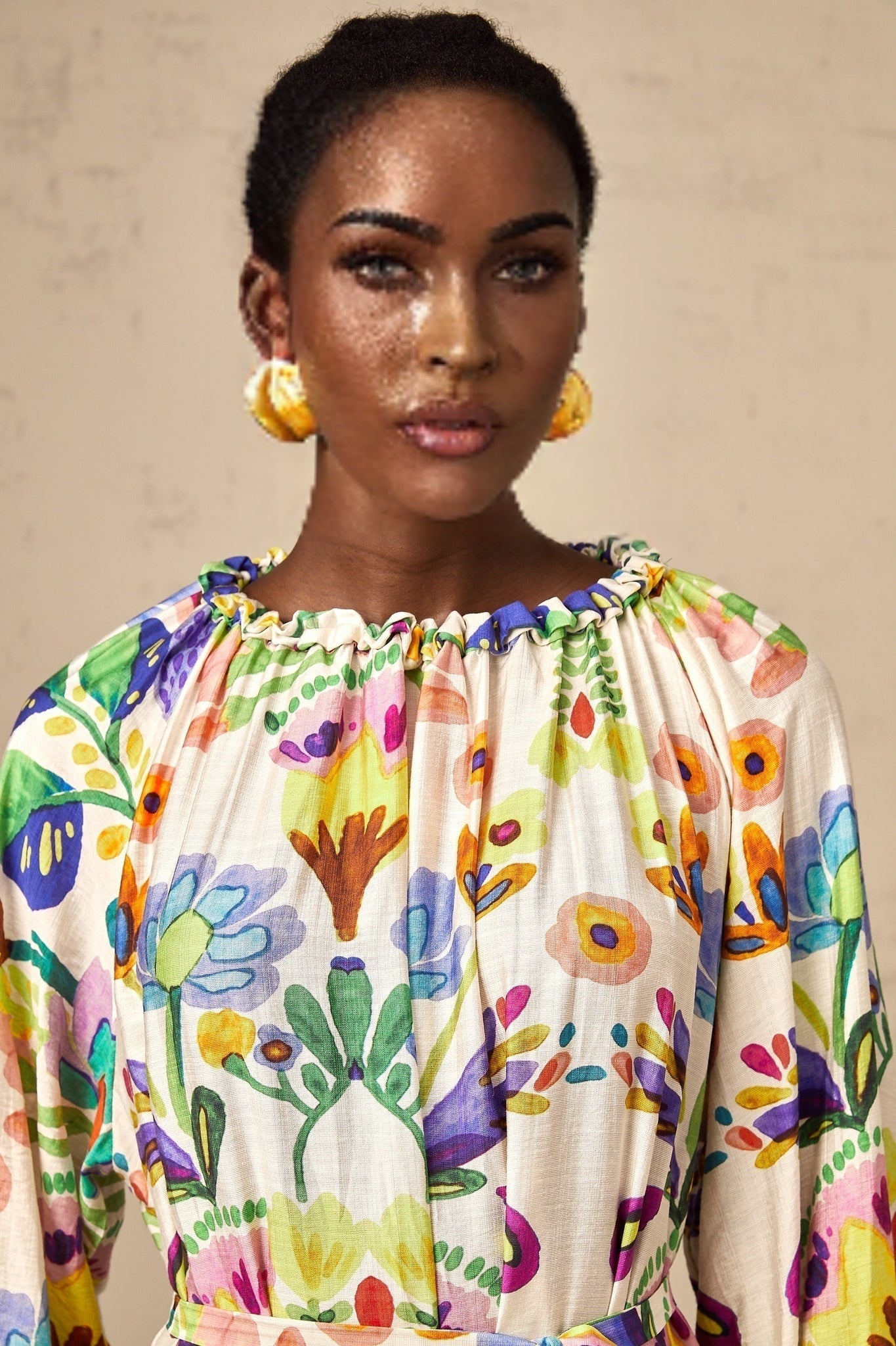 A woman wearing a colorful paisley print midi dress with a fitted bodice and flowing skirt standing against a plain background