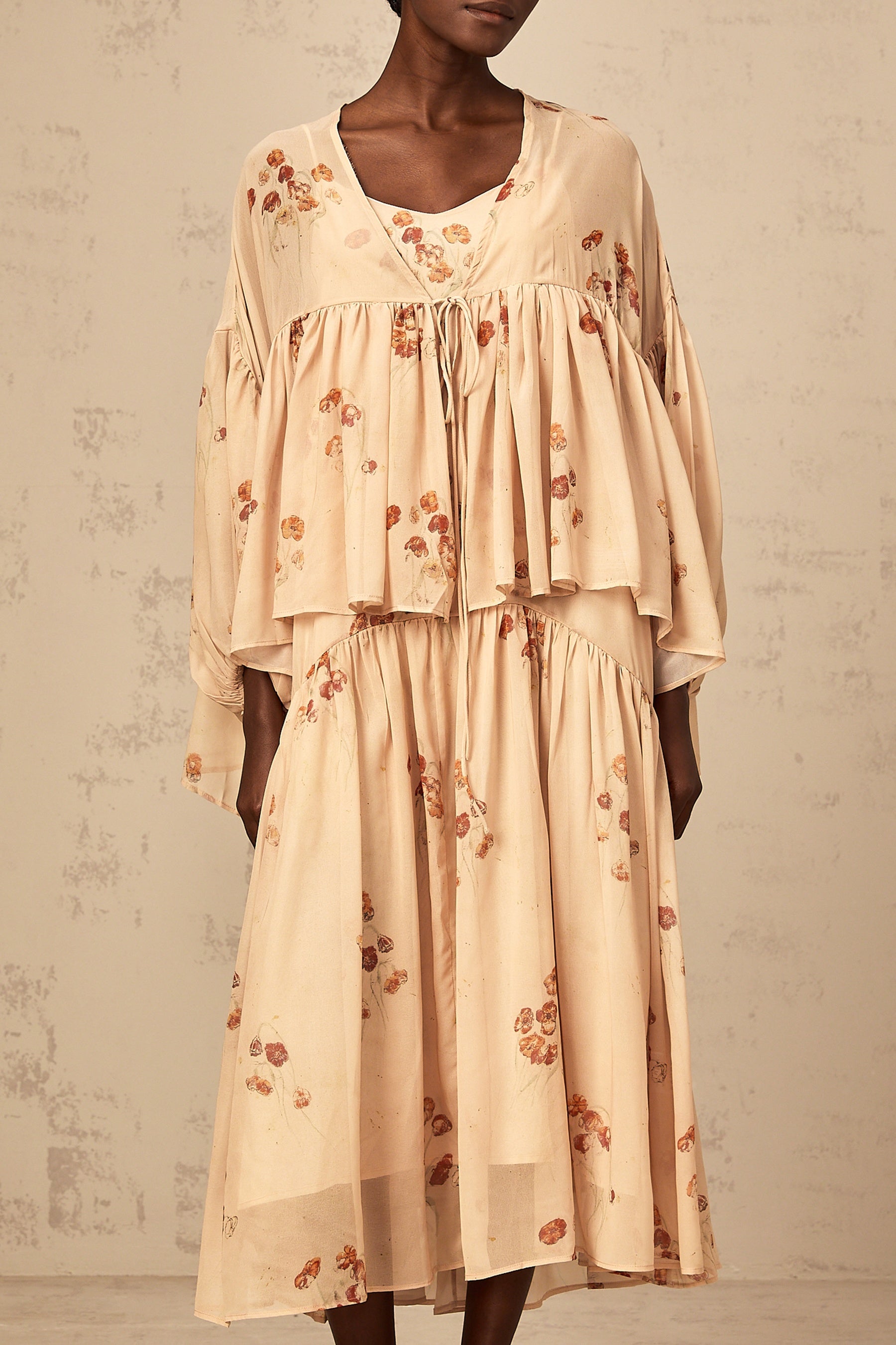 A woman wearing a coralpink floral print matching set consisting of a pleated blouse and dress The outfit has a vibrant pattern and feminine silhouette