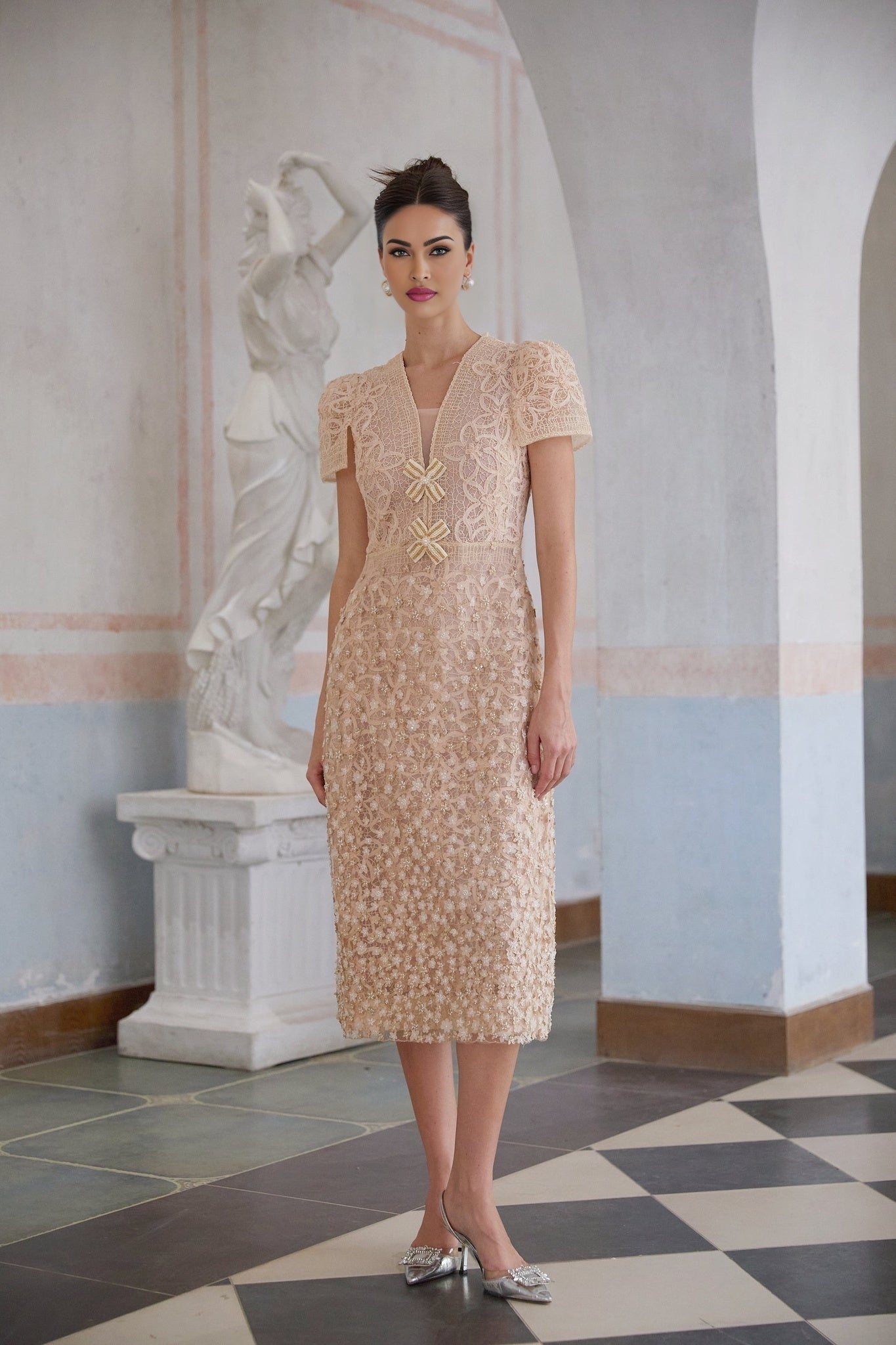 A woman wearing a cream colored crochet midi dress with a floral pattern standing in a neutral background