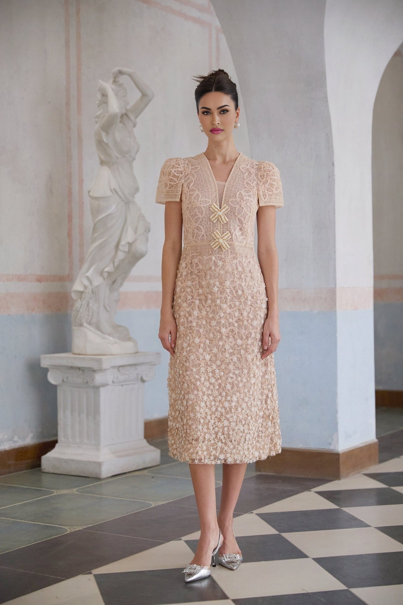 A woman wearing a cream colored midi length dress with a crochet pattern and faux flower details standing in a neutral background