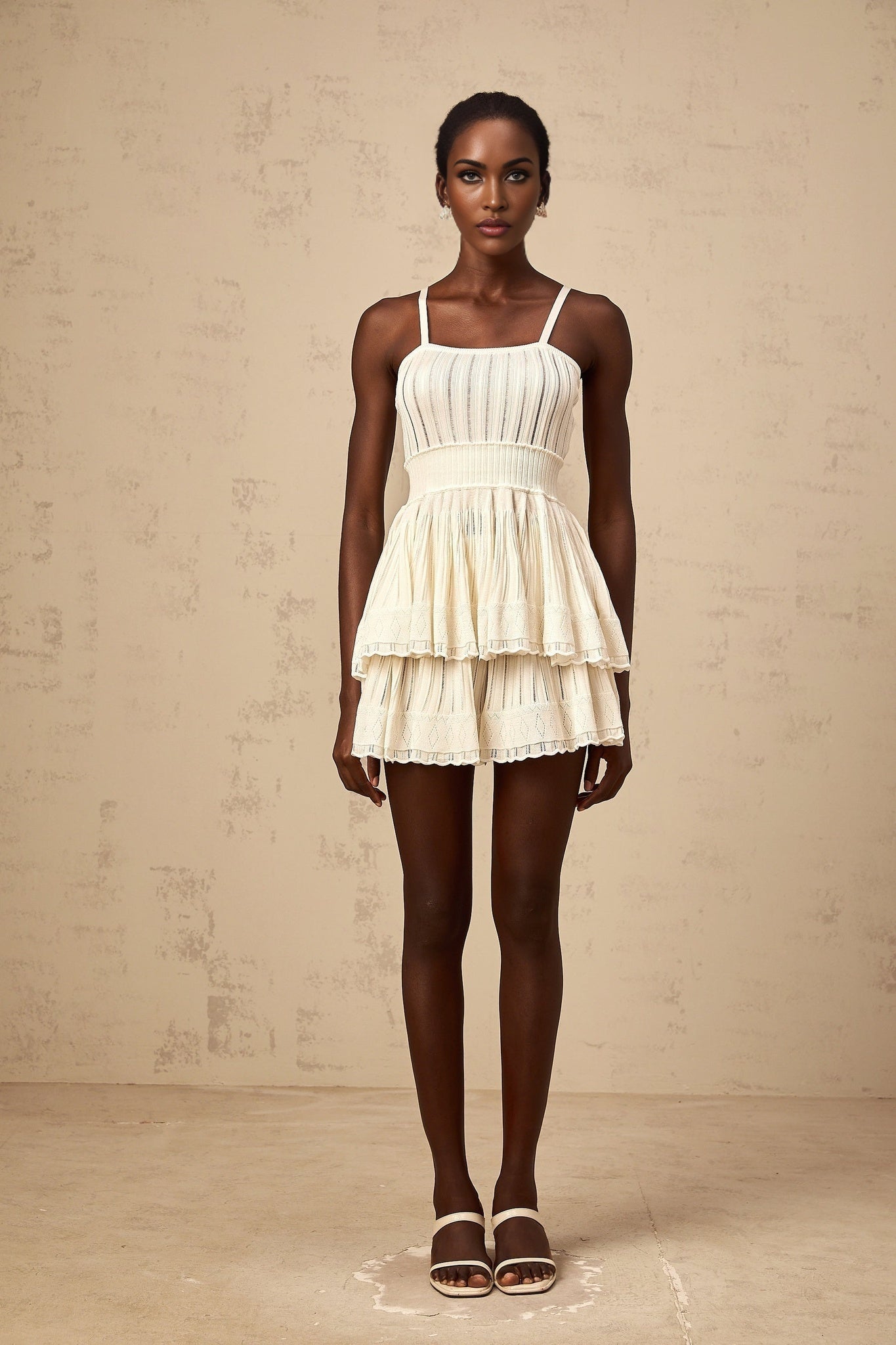 A woman wearing a creamwhite matching set consisting of a shirred crochetknit top and culottes standing against a plain background