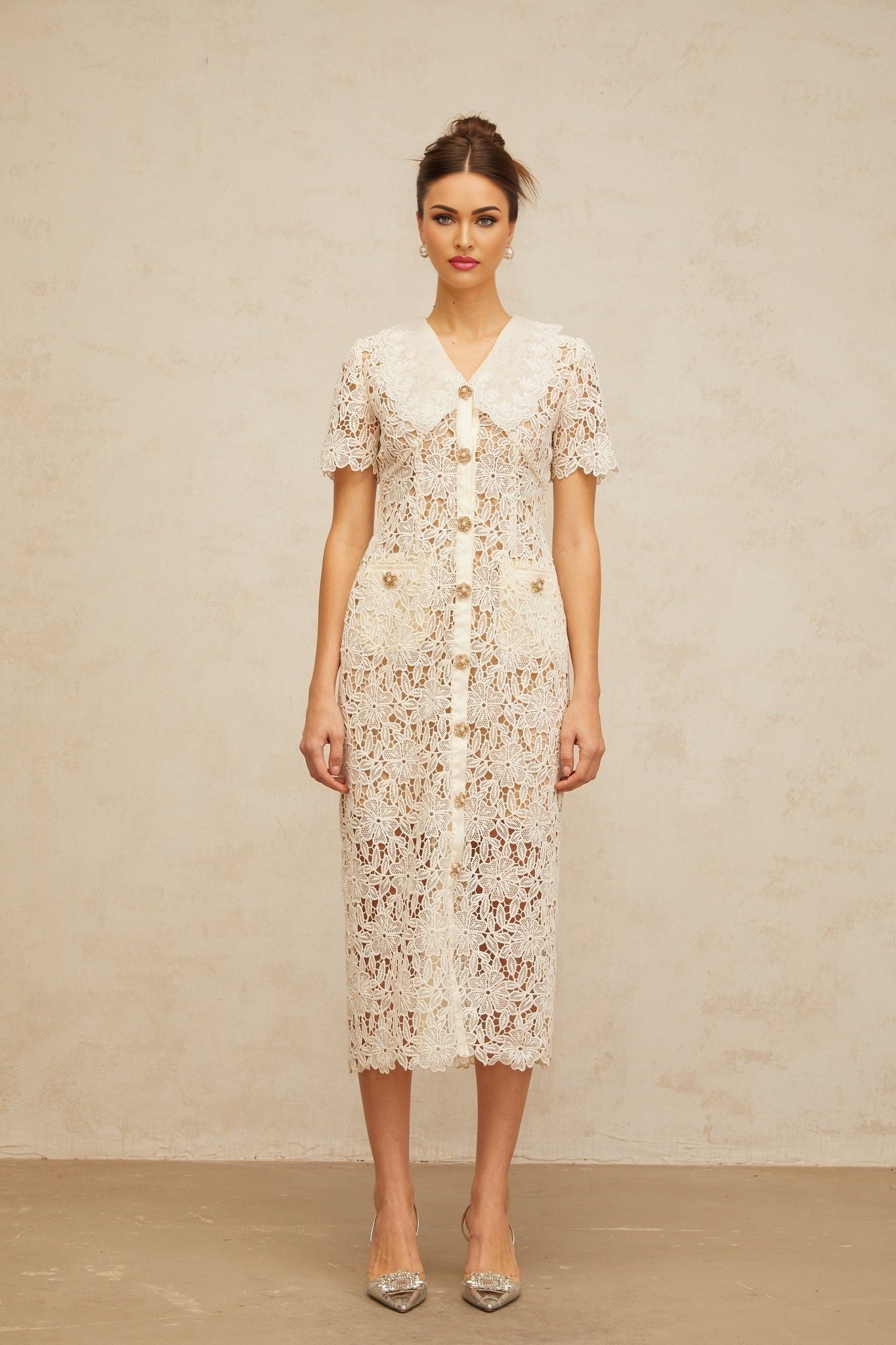 A woman wearing a delicate off white midi dress with corded lace details standing against a plain background
