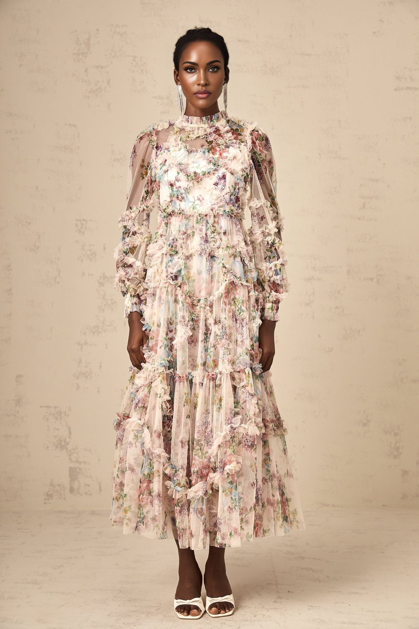 A woman wearing a floral midi dress with ruffled tulle details and a fitted bodice standing in a neutral background