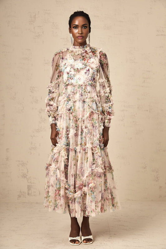 A woman wearing a floral midi dress with ruffled tulle details and a fitted bodice standing in a neutral background