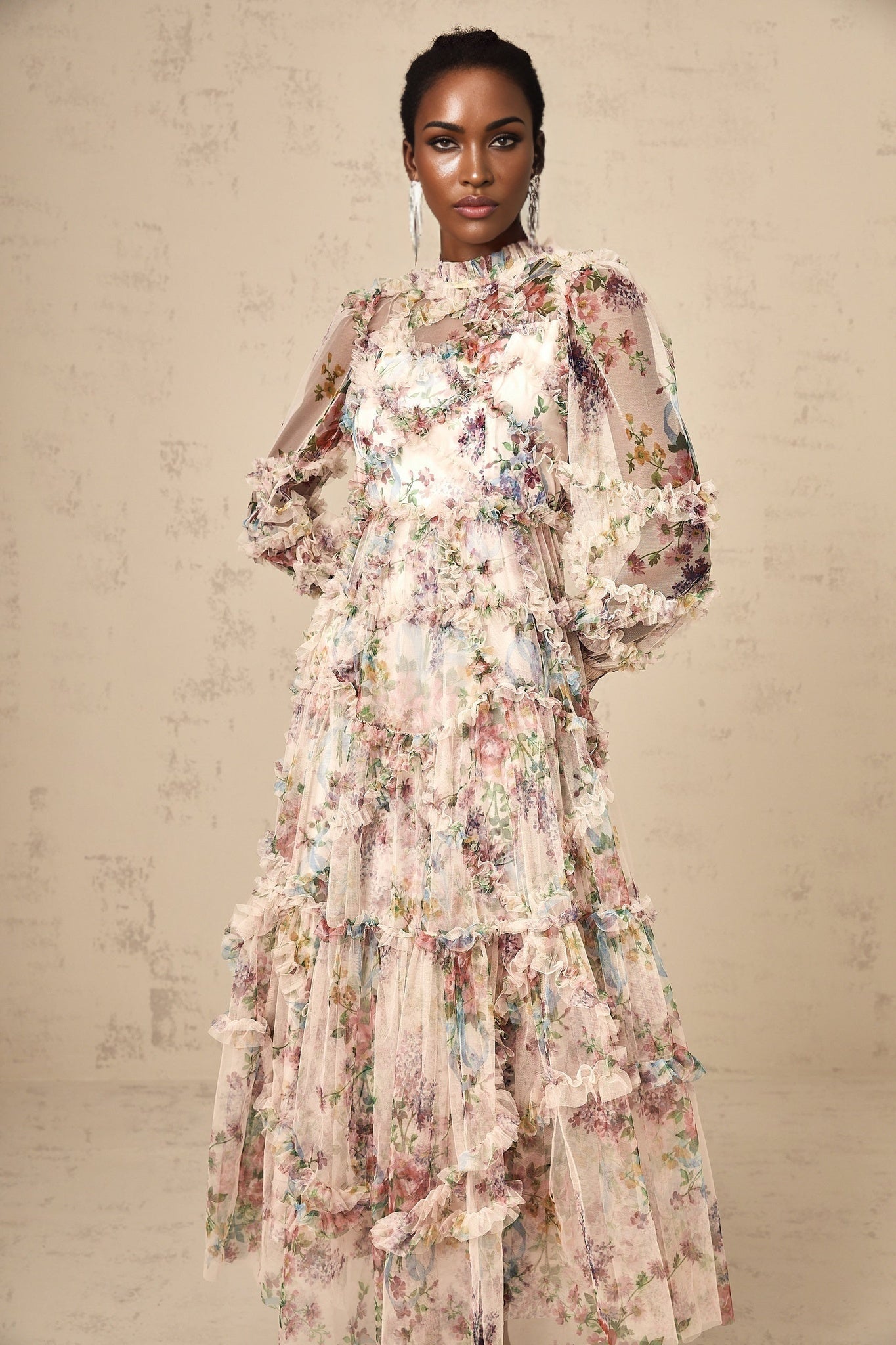 A woman wearing a floral midi dress with ruffled tulle details standing against a plain background