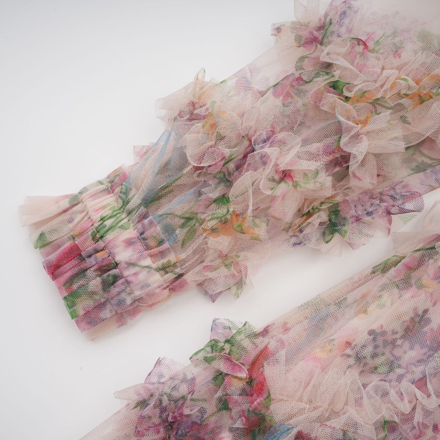 A woman wearing a floral patterned midi dress with ruffled details and a tulle skirt standing against a plain background