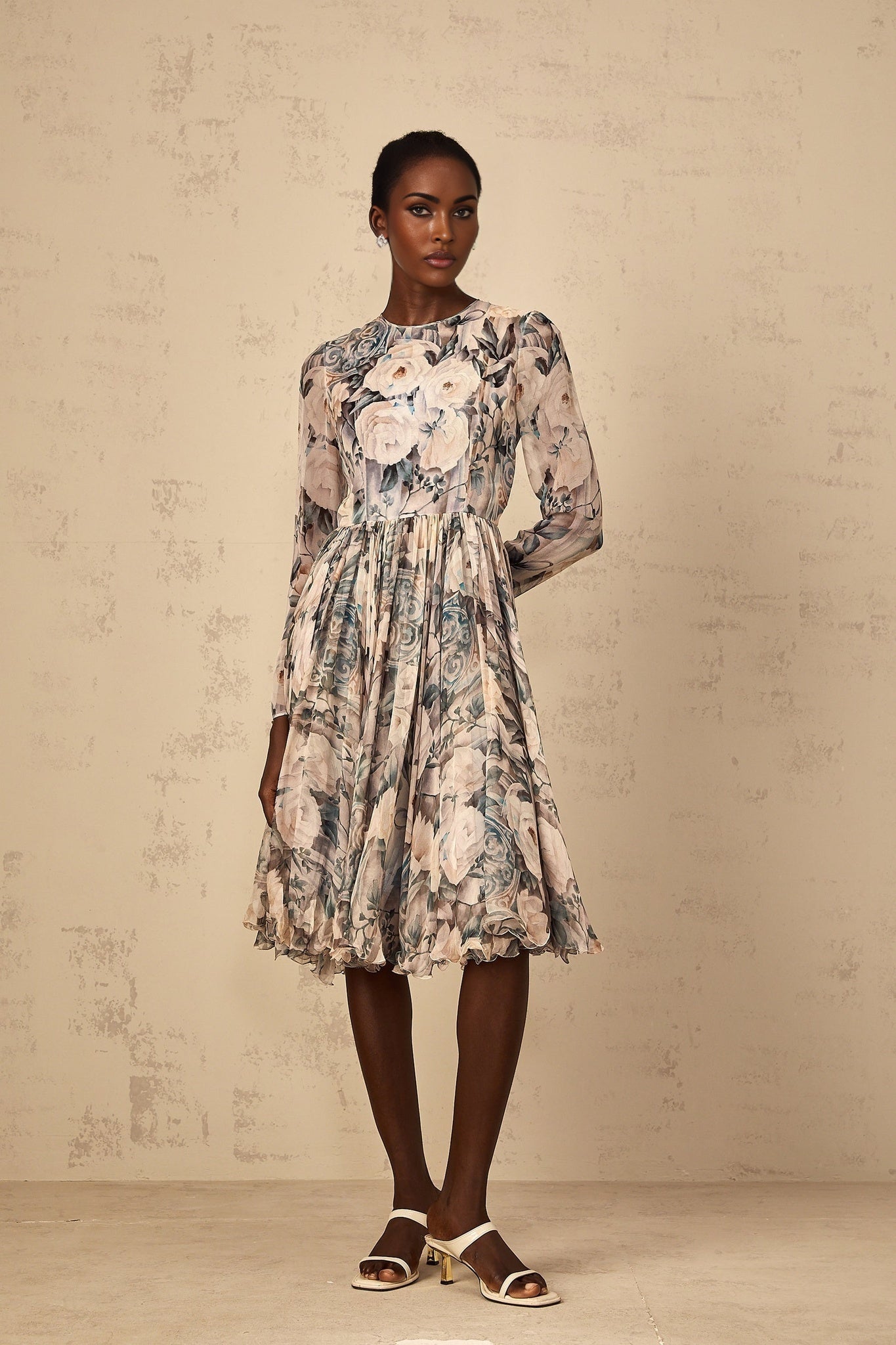 A woman wearing a floral print chiffon midi dress with pleats standing in a casual pose against a plain background