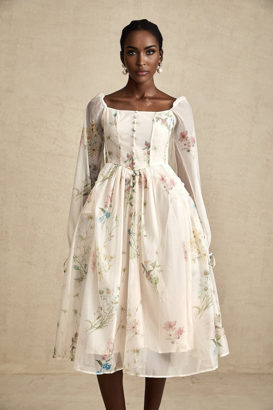 A woman wearing a floral print midi dress with a square neckline and short sleeves standing against a plain background