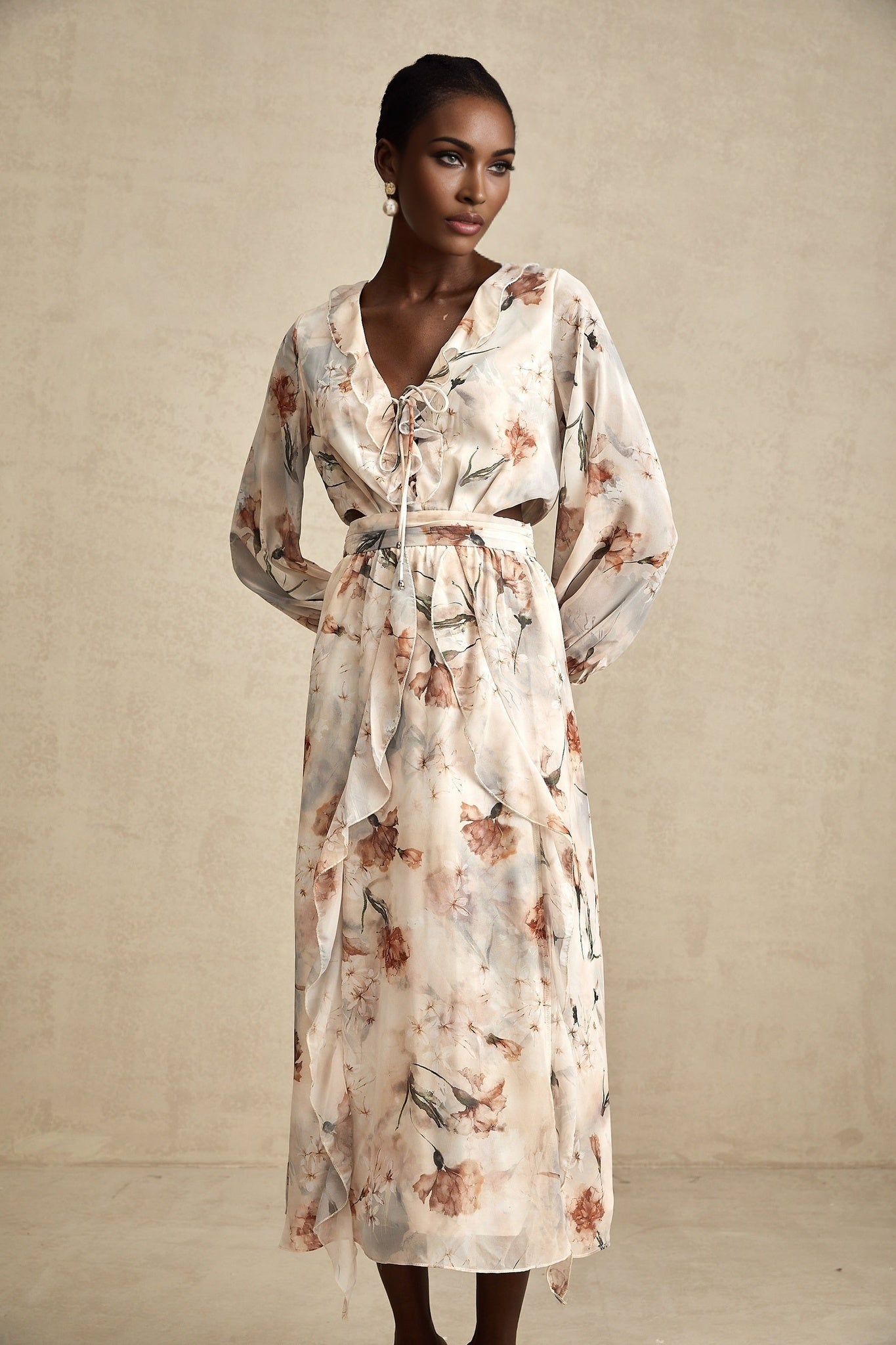 A woman wearing a floral print midi dress with an open waist design The dress features a colorful flower pattern on a light background and has a flowing silhouette that falls to mid calf length