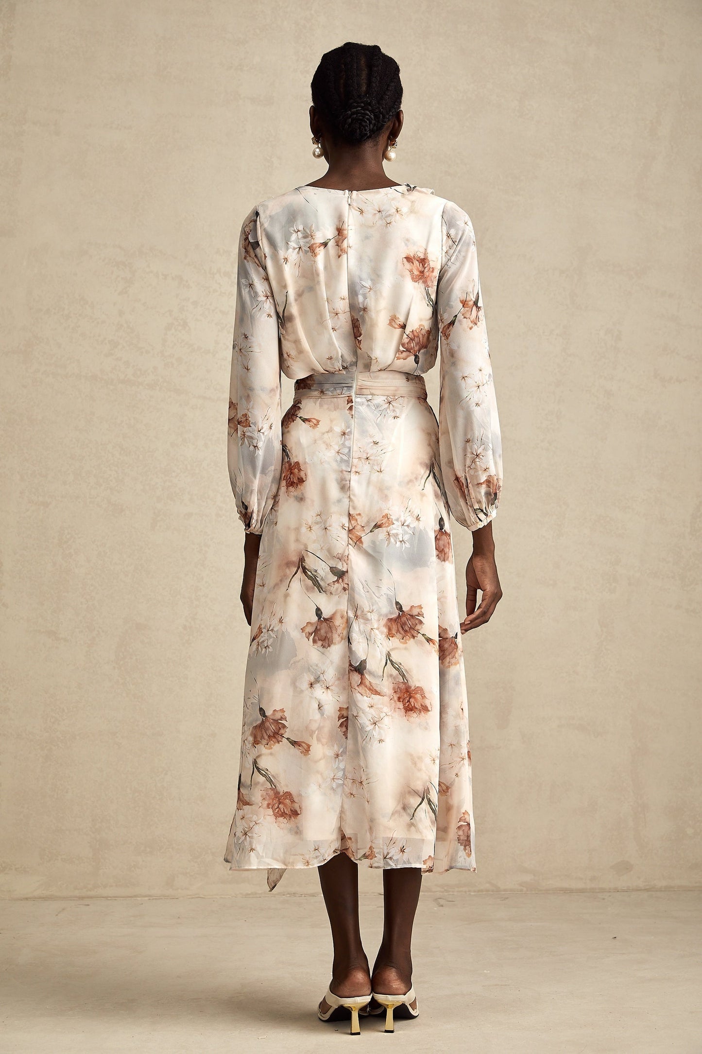 A woman wearing a floral print midi dress with an open waist design The dress has a colorful floral pattern on a light background It features long sleeves and a flowing skirt that falls to mid calf length The open waist detail adds a stylish and flattering touch to the silhouette