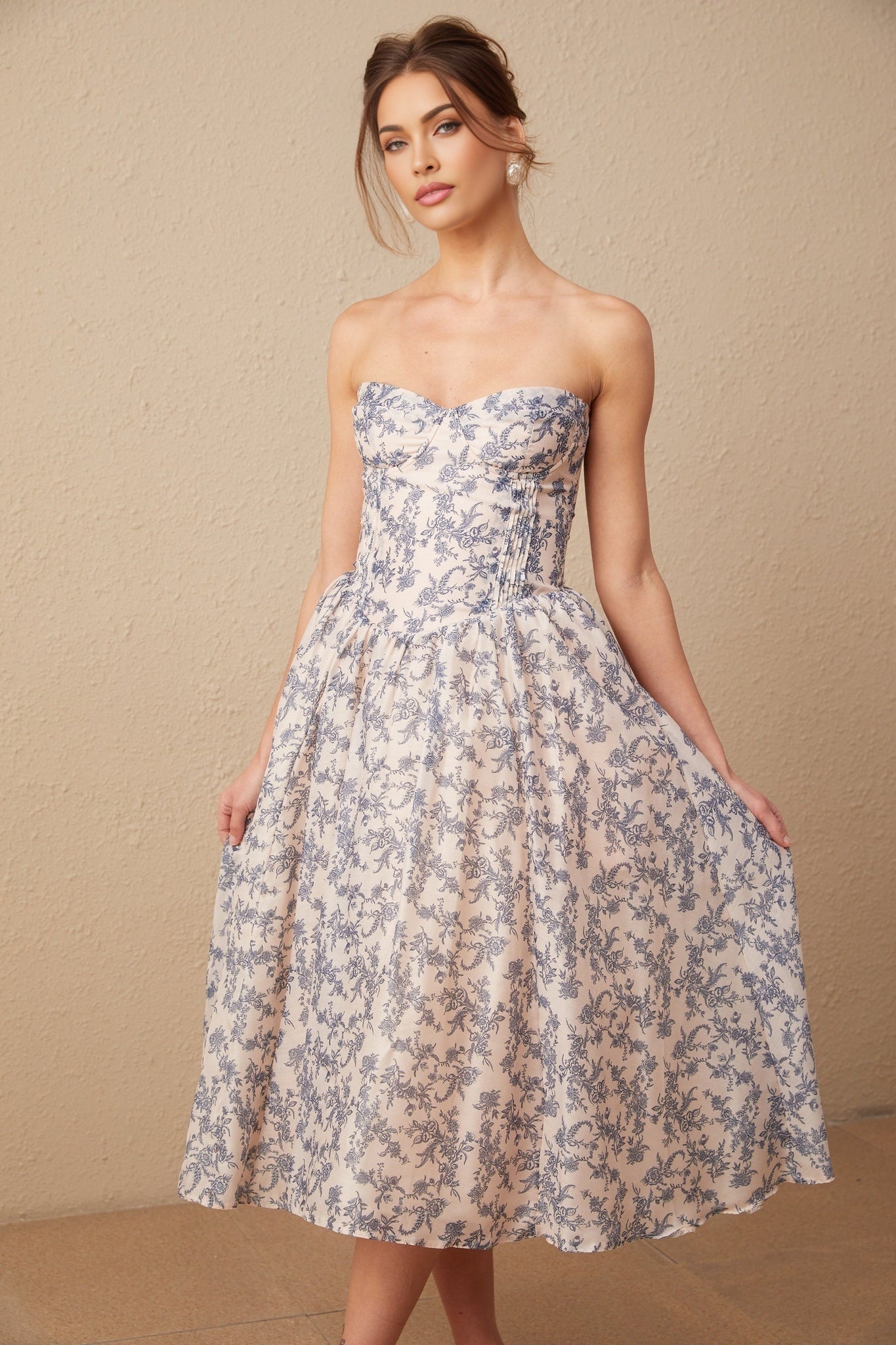 A woman wearing a floral print off shoulder midi dress with a fitted bodice and flowy skirt standing in a casual pose