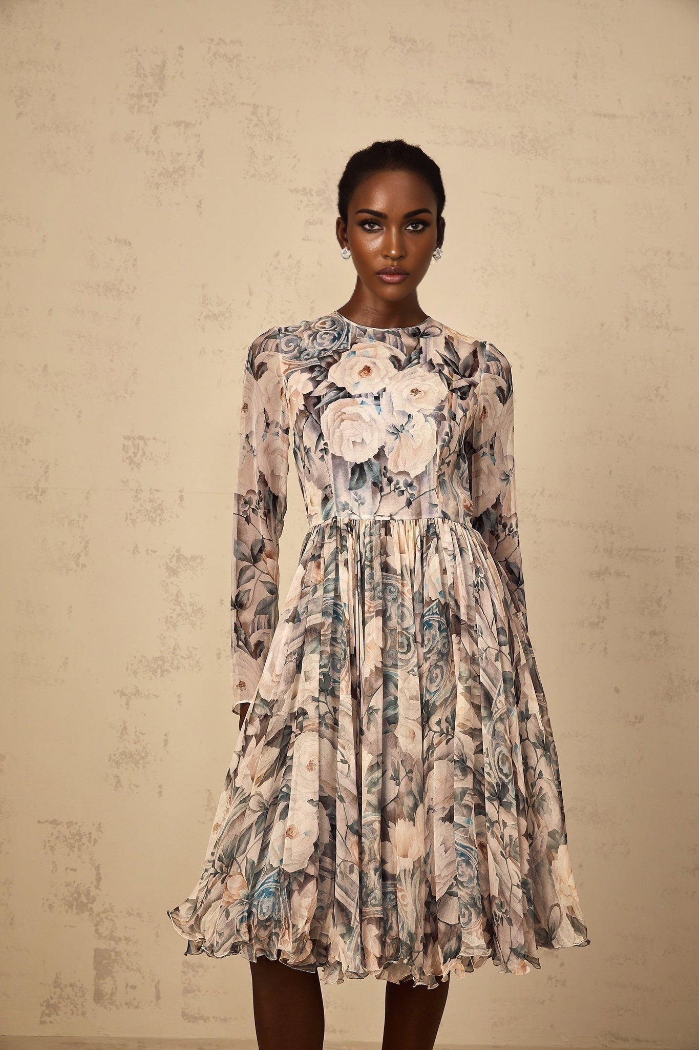 A woman wearing a floral print pleated chiffon midi dress with a flowing silhouette standing against a plain background