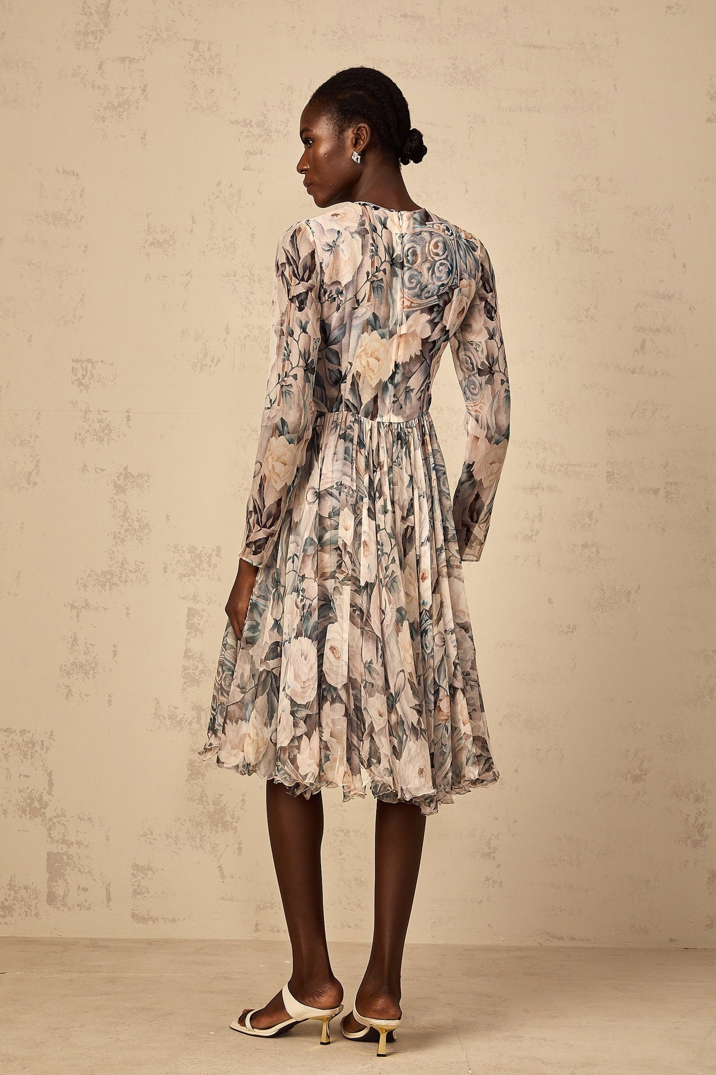 A woman wearing a floral print pleated chiffon midi dress with a flowing silhouette standing against a plain background