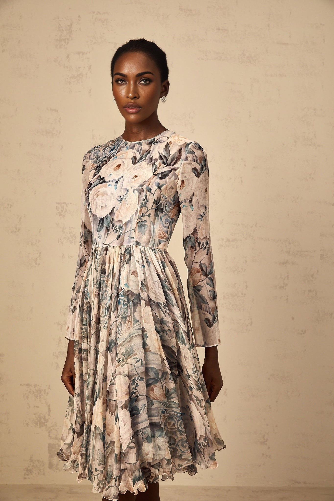 A woman wearing a floral print pleated chiffon midi dress with a flowing skirt and delicate pattern standing in a casual pose against a plain background