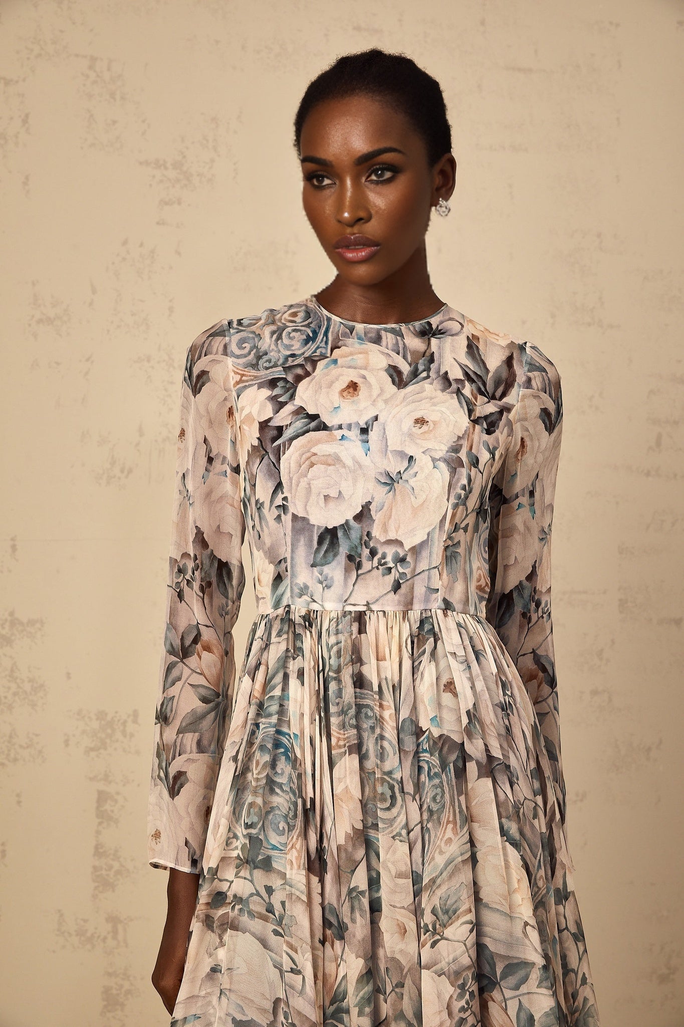 A woman wearing a floral print pleated chiffon midi dress with a soft flowing silhouette standing against a plain background
