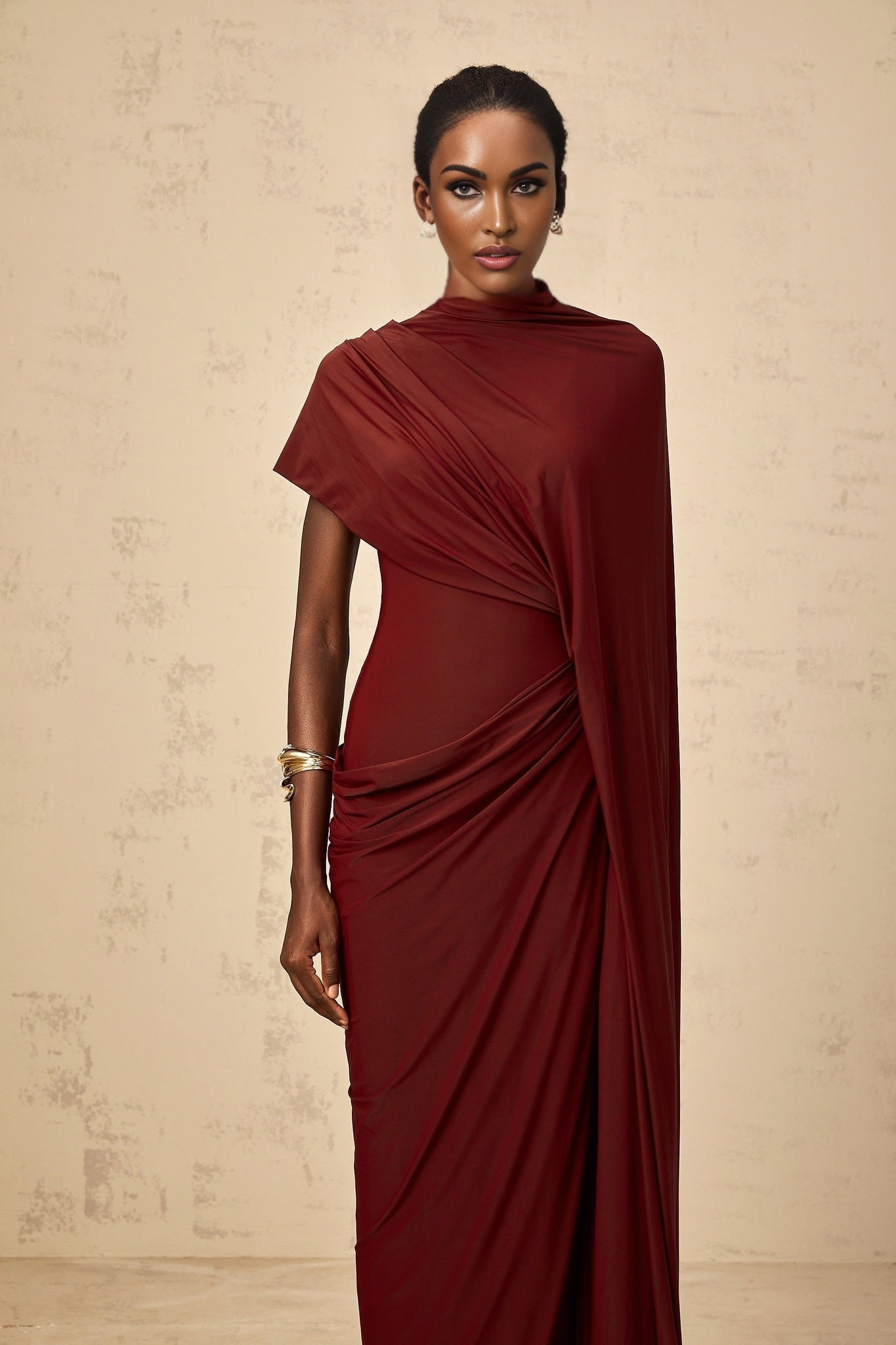 A woman wearing a flowing asymmetrical cape and matching dress in a draped style The ensemble is called Fenella and features a coordinated design with elegant draping