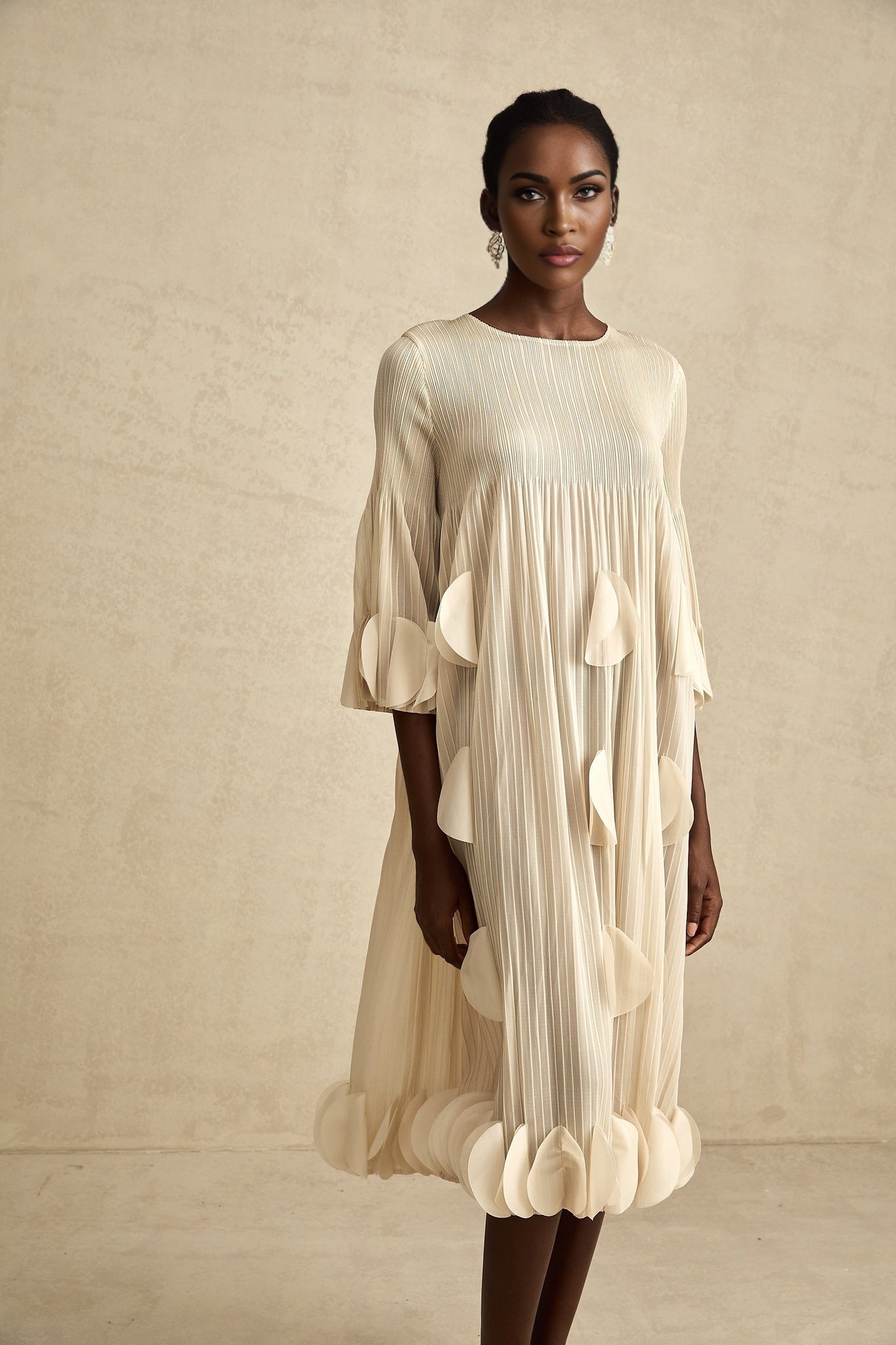 A woman wearing a flowy midi dress with three dimensional petallike pleats in a graceful silhouette