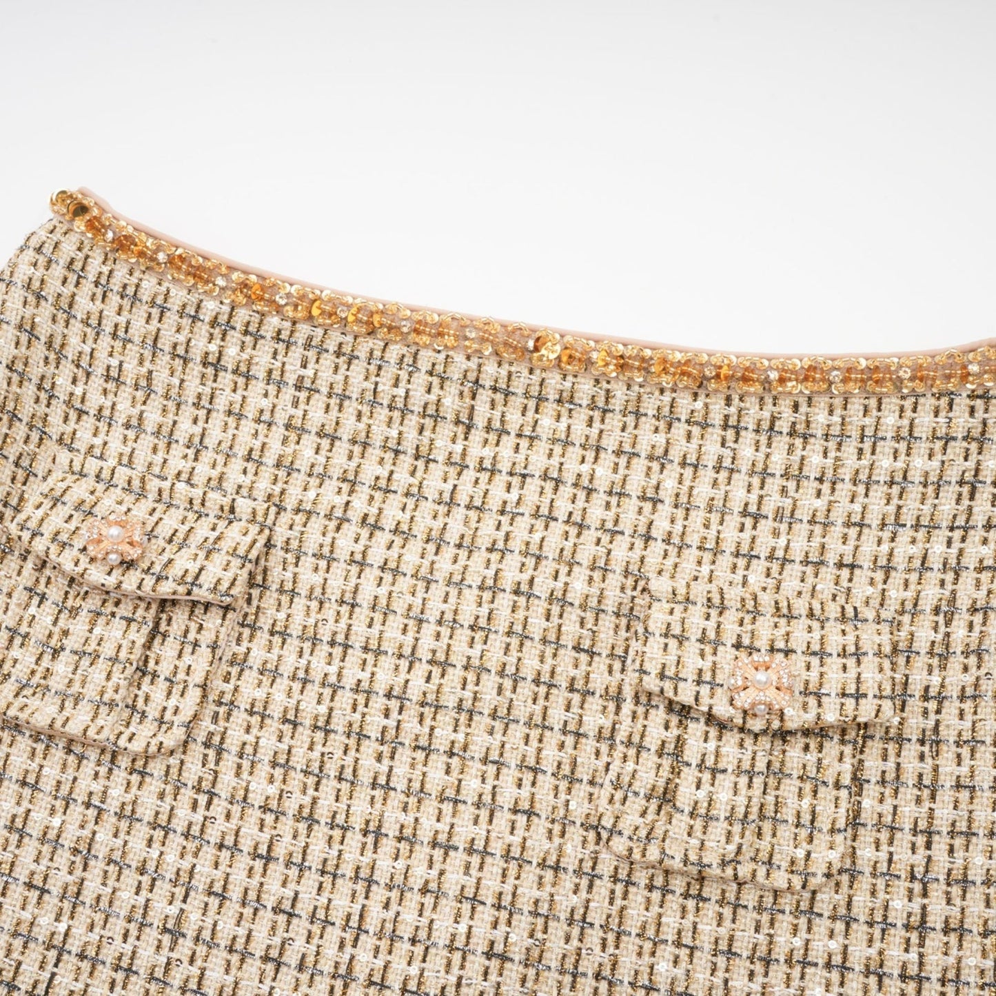 A woman wearing a gold tweed jacket and matching skirt set with sequin embellishments The outfit shimmers in the light and has a luxurious texture
