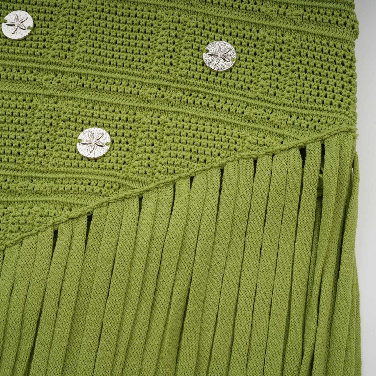 A woman wearing a green knitted two piece outfit consisting of a top and skirt with embellishments The top has short sleeves and the skirt falls to mid thigh length The set is called Annette and is designed to be worn as a matching ensemble