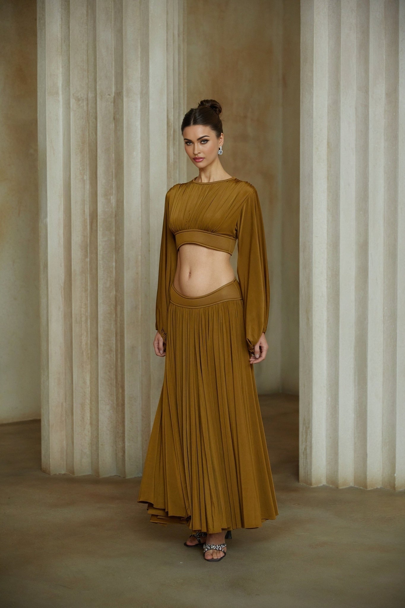 A woman wearing a green two piece outfit consisting of a fully pleated blouse and matching pleated skirt standing in a relaxed pose