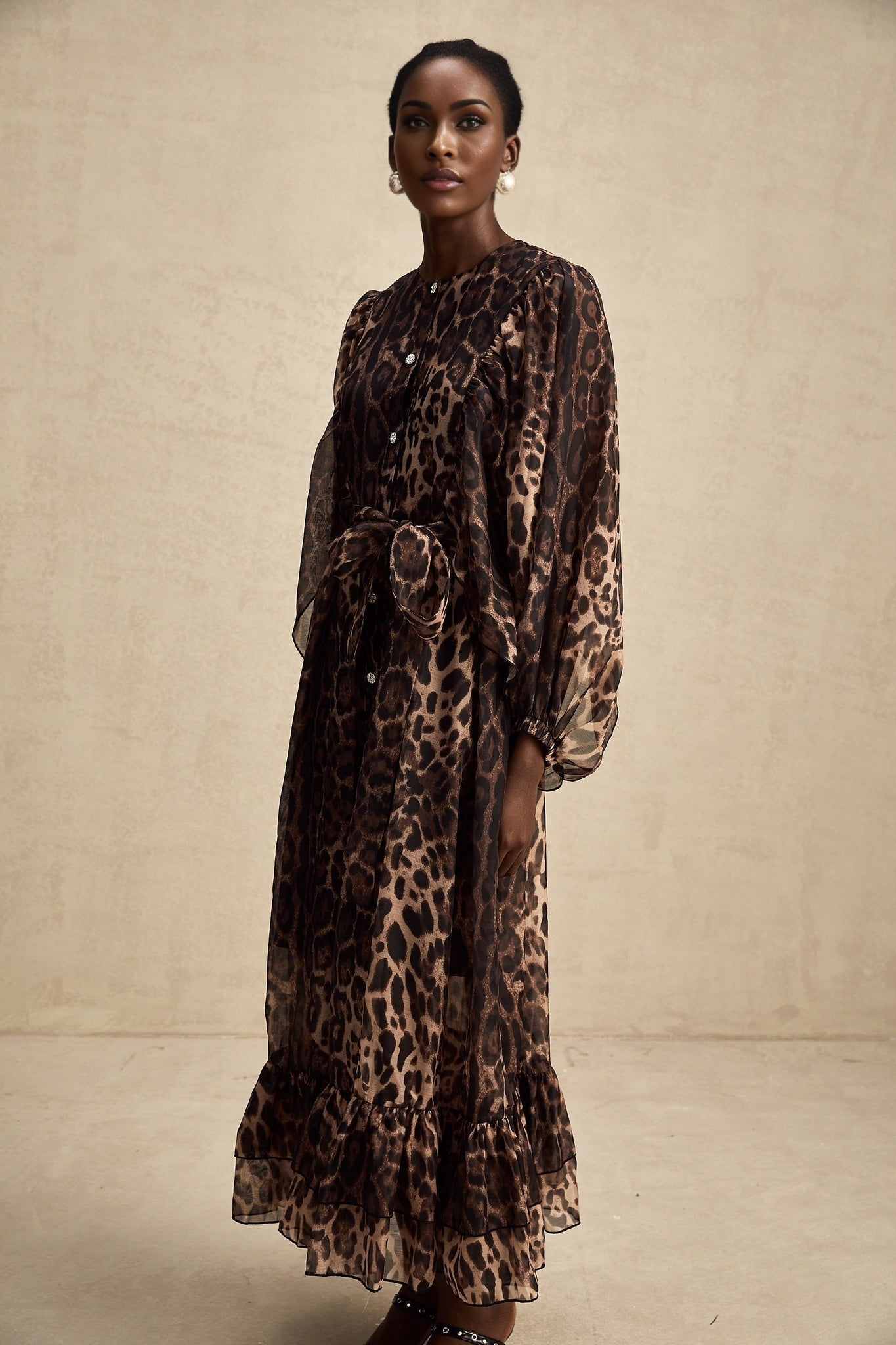 A woman wearing a leopard print midi dress with a single breasted design The dress features long sleeves and a fitted silhouette reaching below the knees