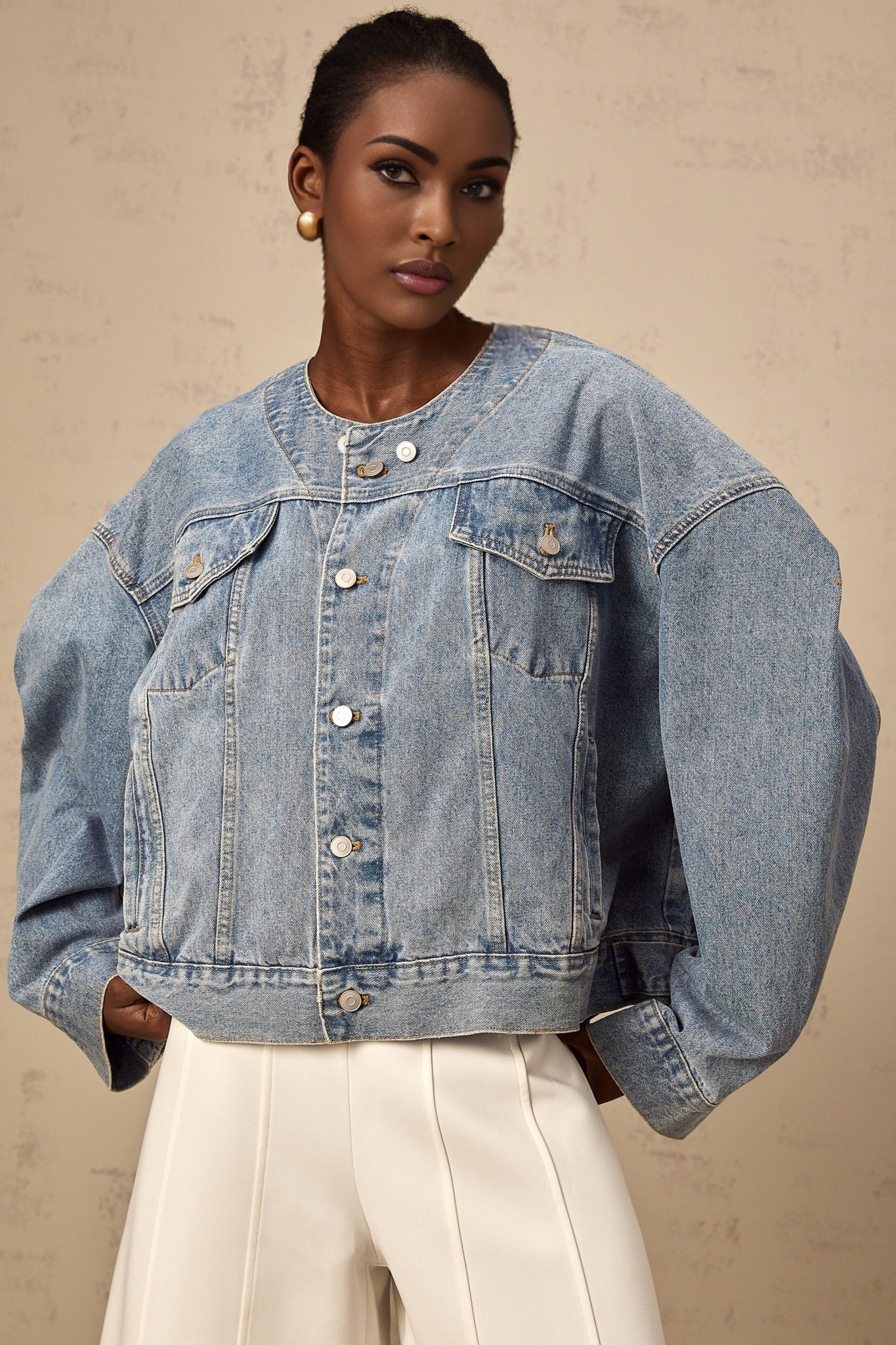 A woman wearing a light blue collarless denim jacket with front pockets and button closure