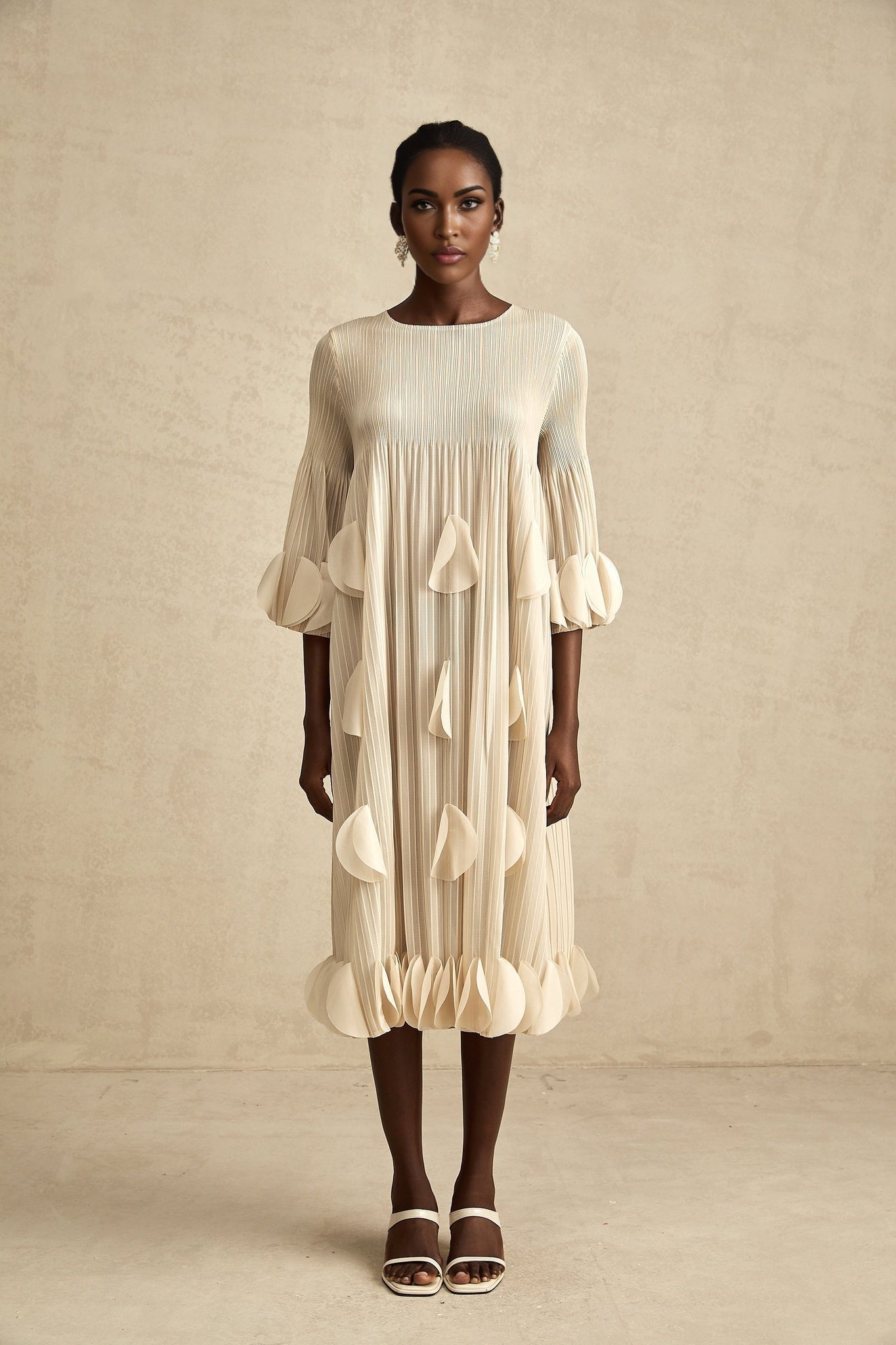 A woman wearing a light blue midi dress with three dimensional pleated petals covering the entire garment creating a floral textured effect