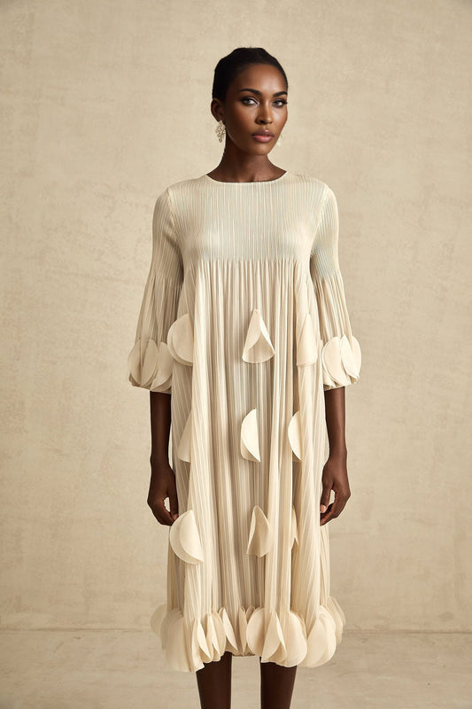 A woman wearing a light colored midi dress with 3d petal pleated details standing in a relaxed pose
