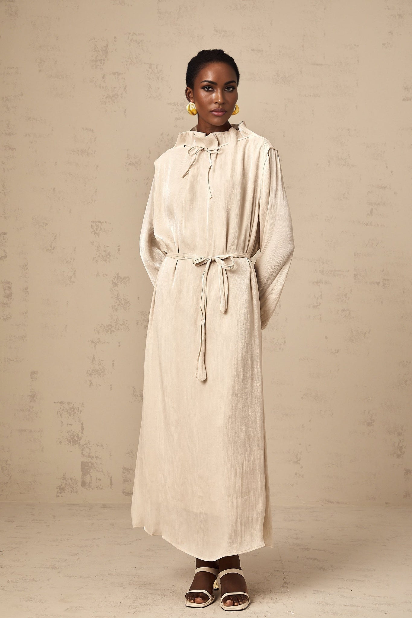 A woman wearing a light colored tulle midi dress with a self tie waist standing in a neutral background
