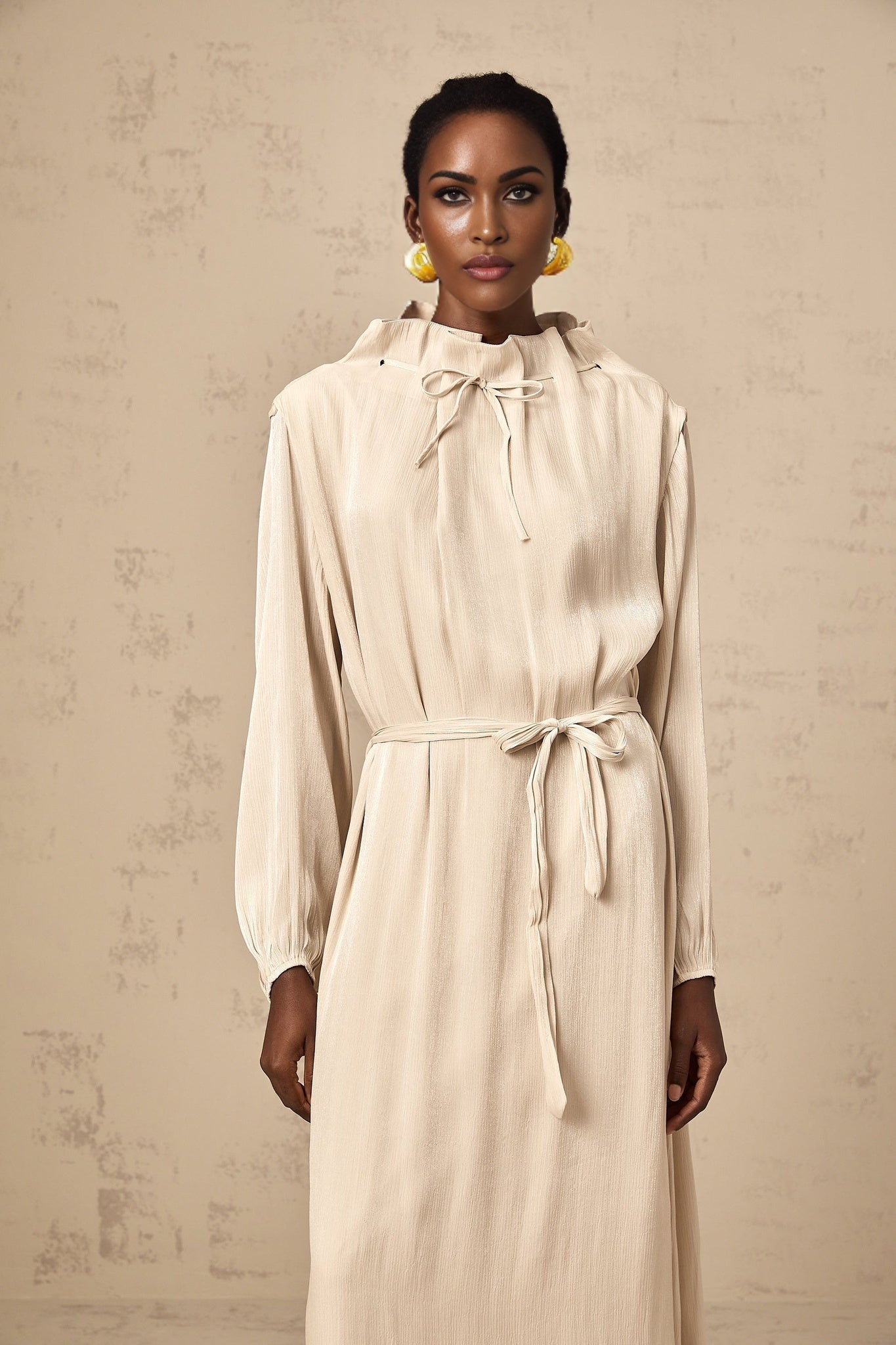 A woman wearing a light colored tulle midi dress with a self tie waist standing in a relaxed pose against a plain background