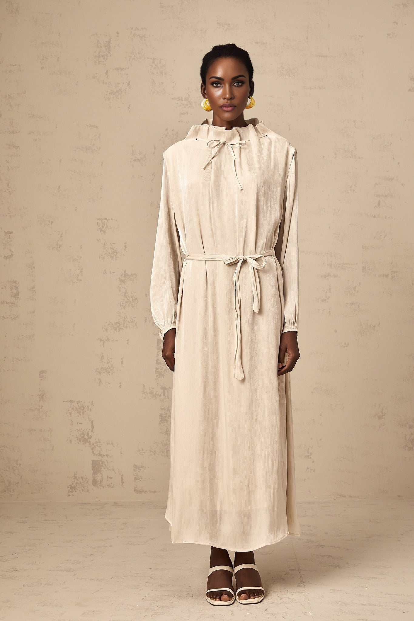 A woman wearing a lightcolored tulle midi dress with a selftie waist standing in a neutral backdrop